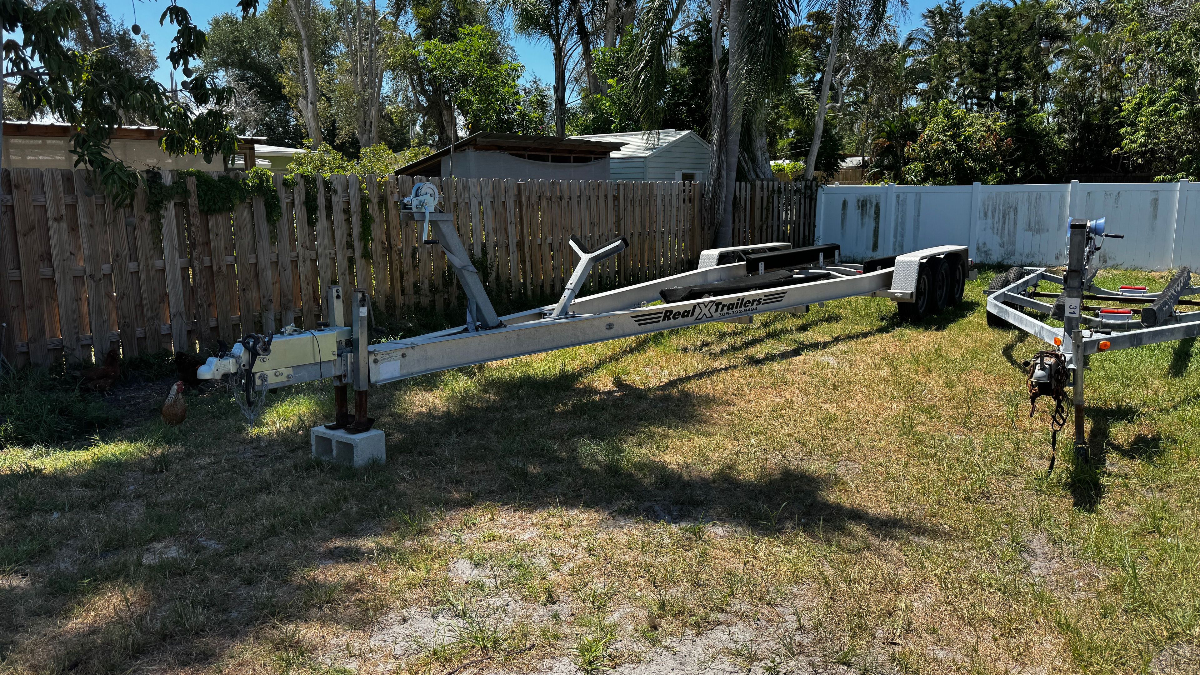 Boat trailer on a grassy lot next to a wooden fence.