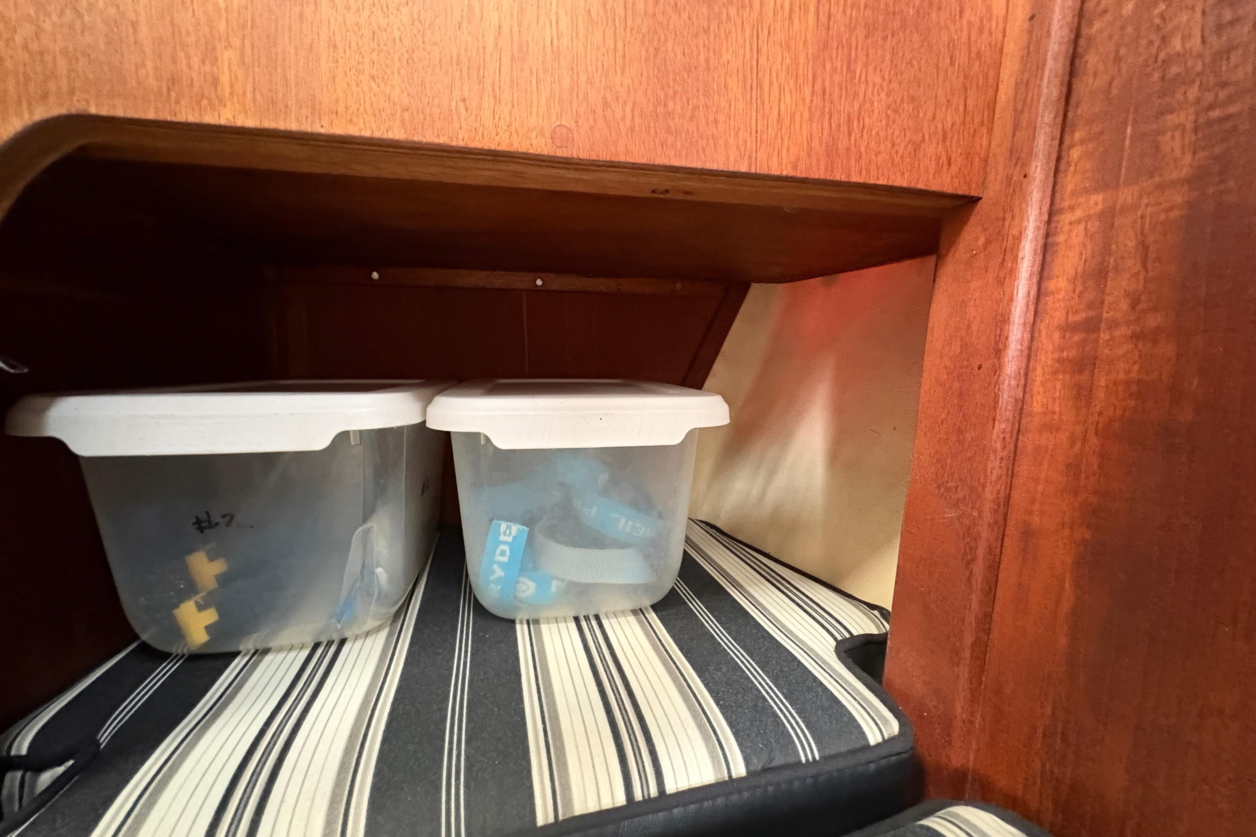 Storage area in 1981 Sabre 31 sailboat with plastic containers and striped cushion.
