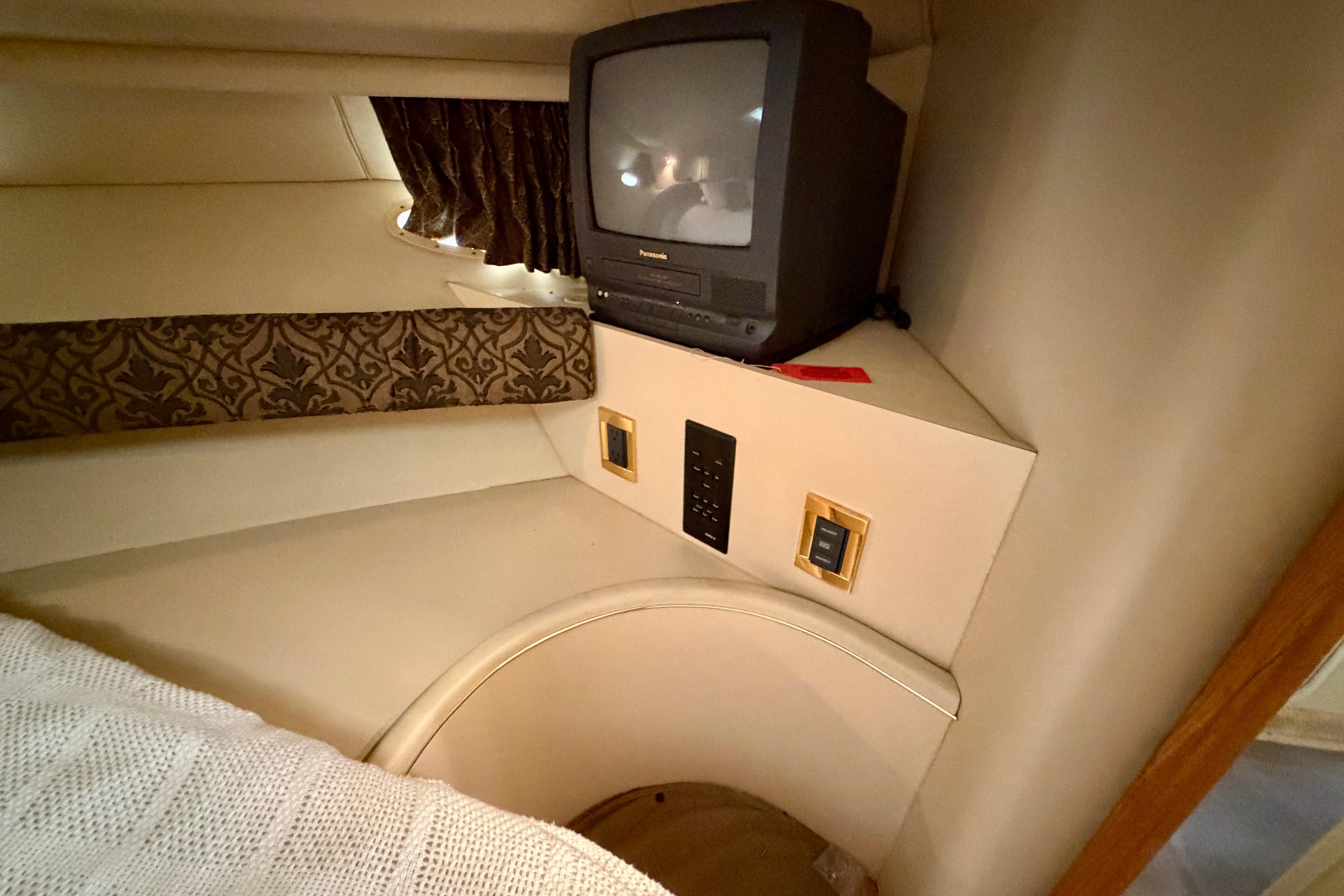 1999 Sea Ray 400 Sundancer cabin with vintage TV and patterned curtains.