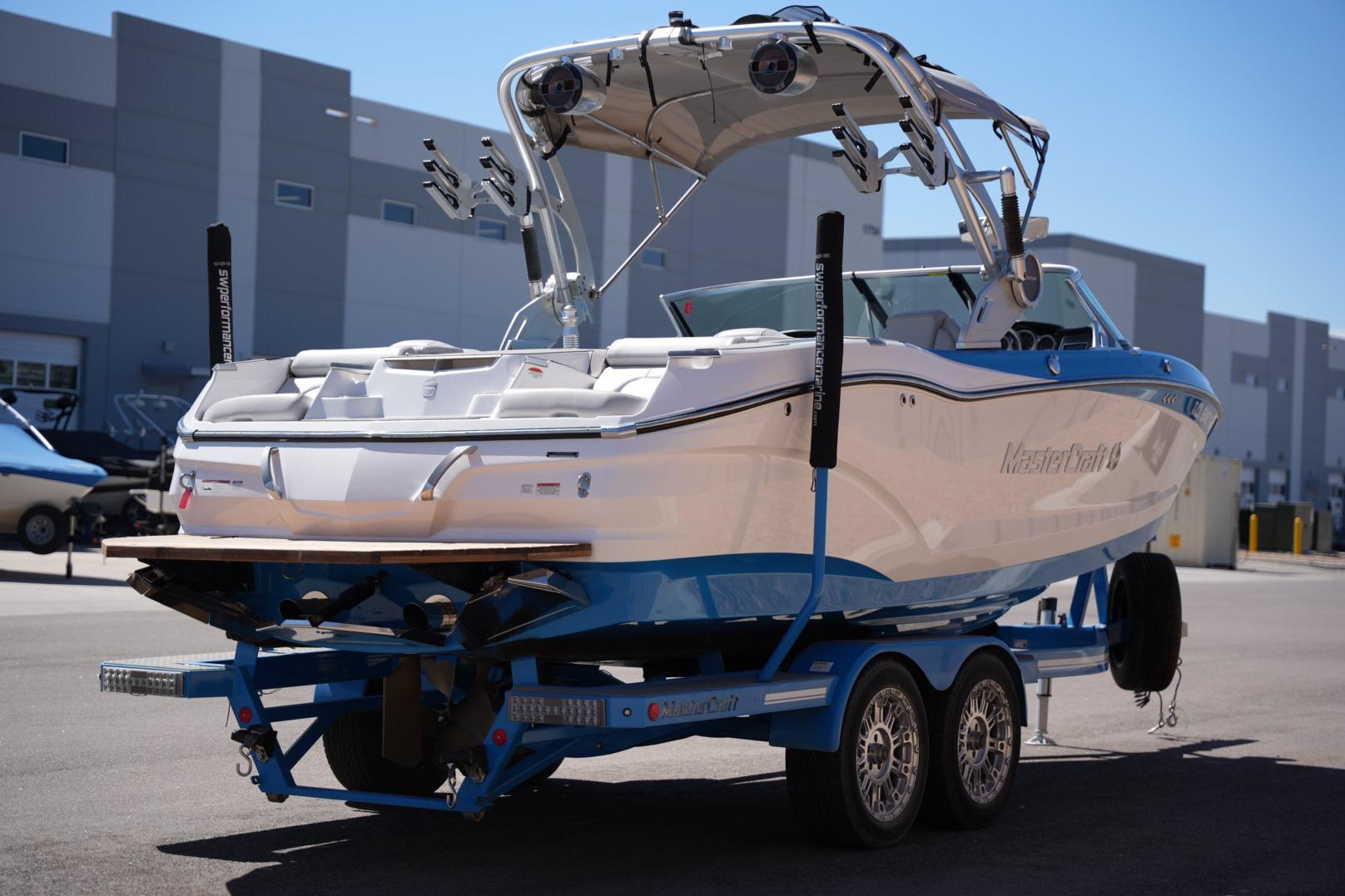 2020 MasterCraft X22 boat on trailer, parked outdoors near industrial buildings.