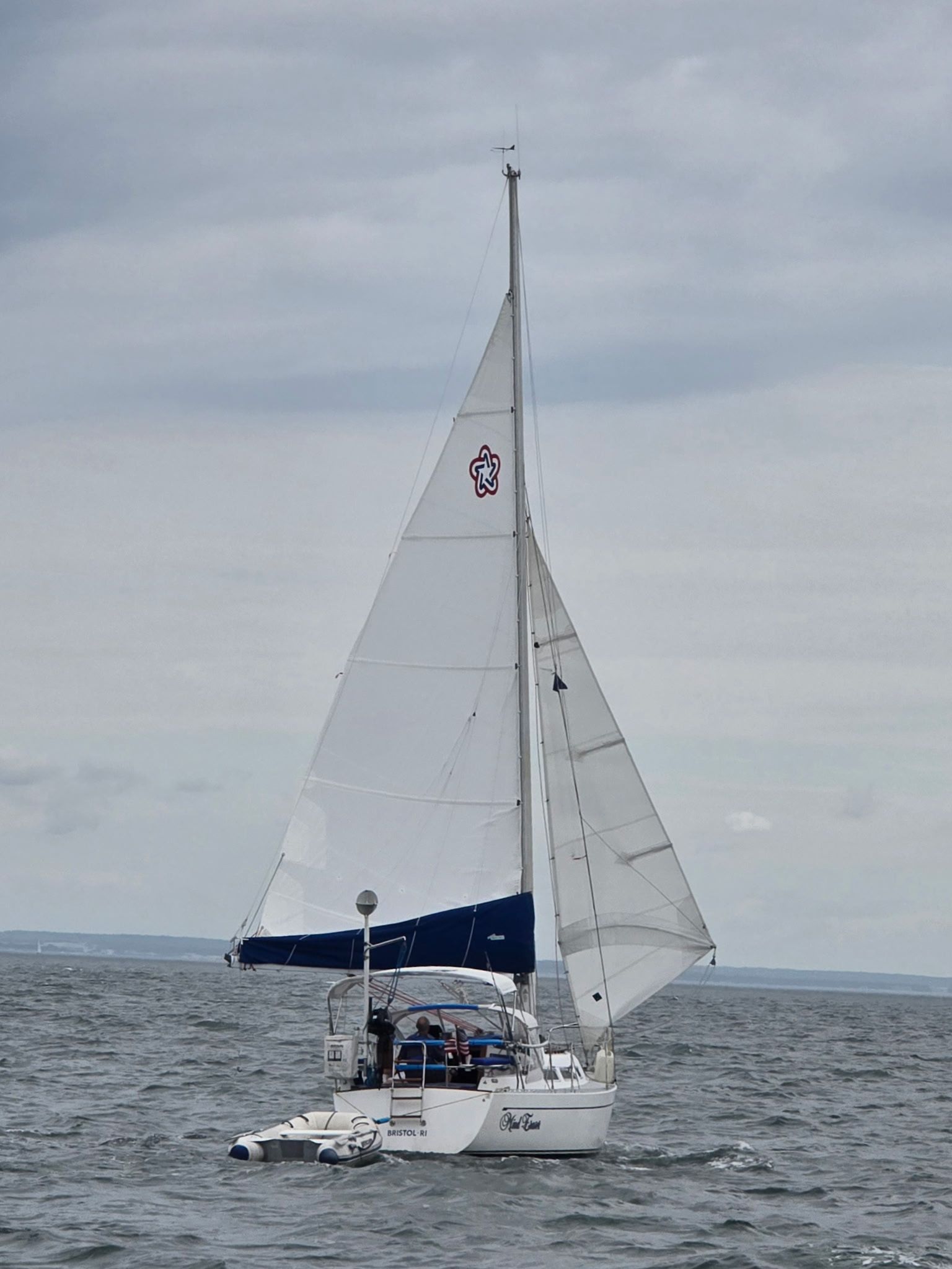 A sailboat with white sails on calm water under a cloudy sky.