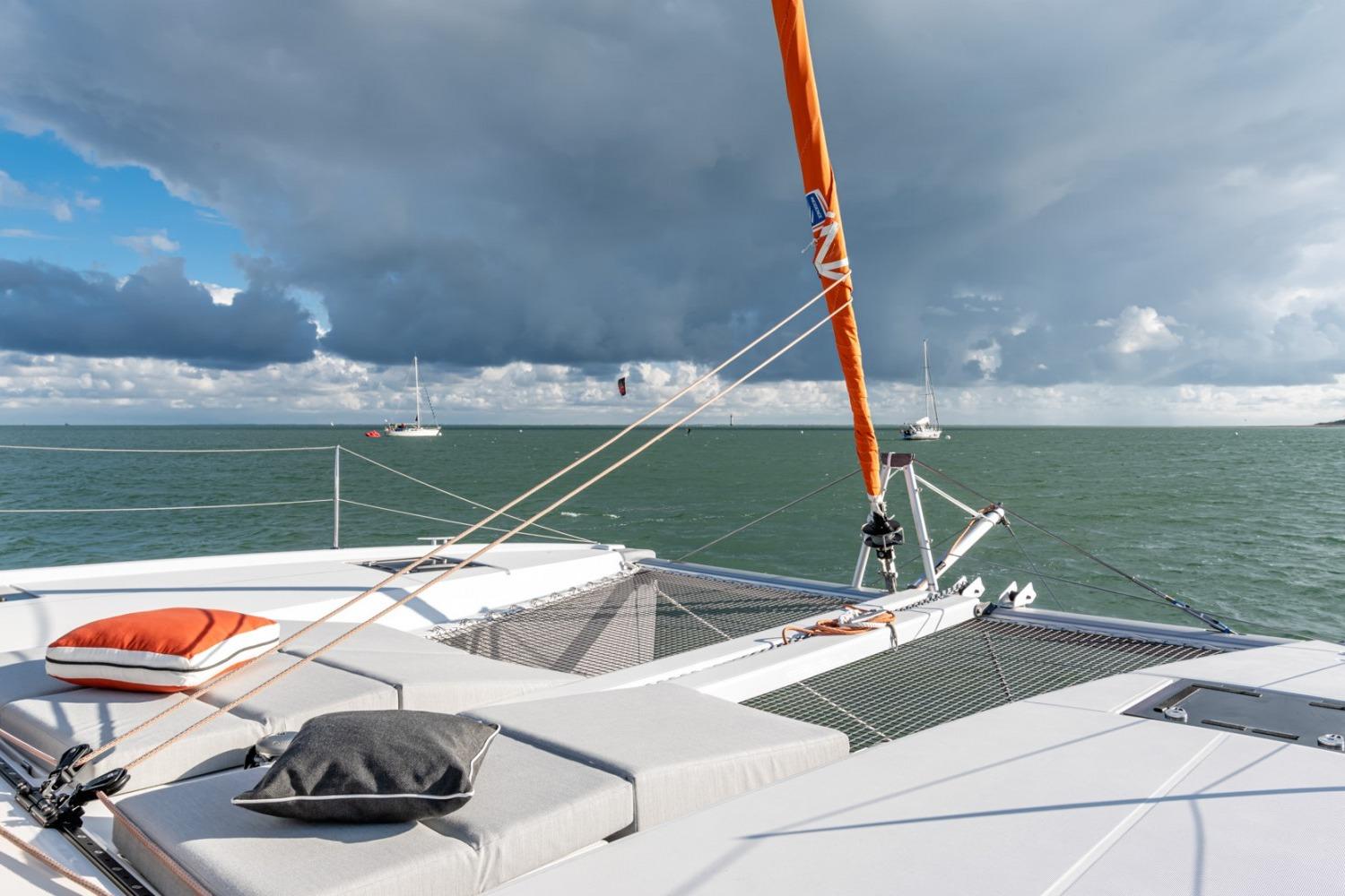 2024 Excess EXCESS 11 catamaran deck with cushions, sailing on a cloudy day.