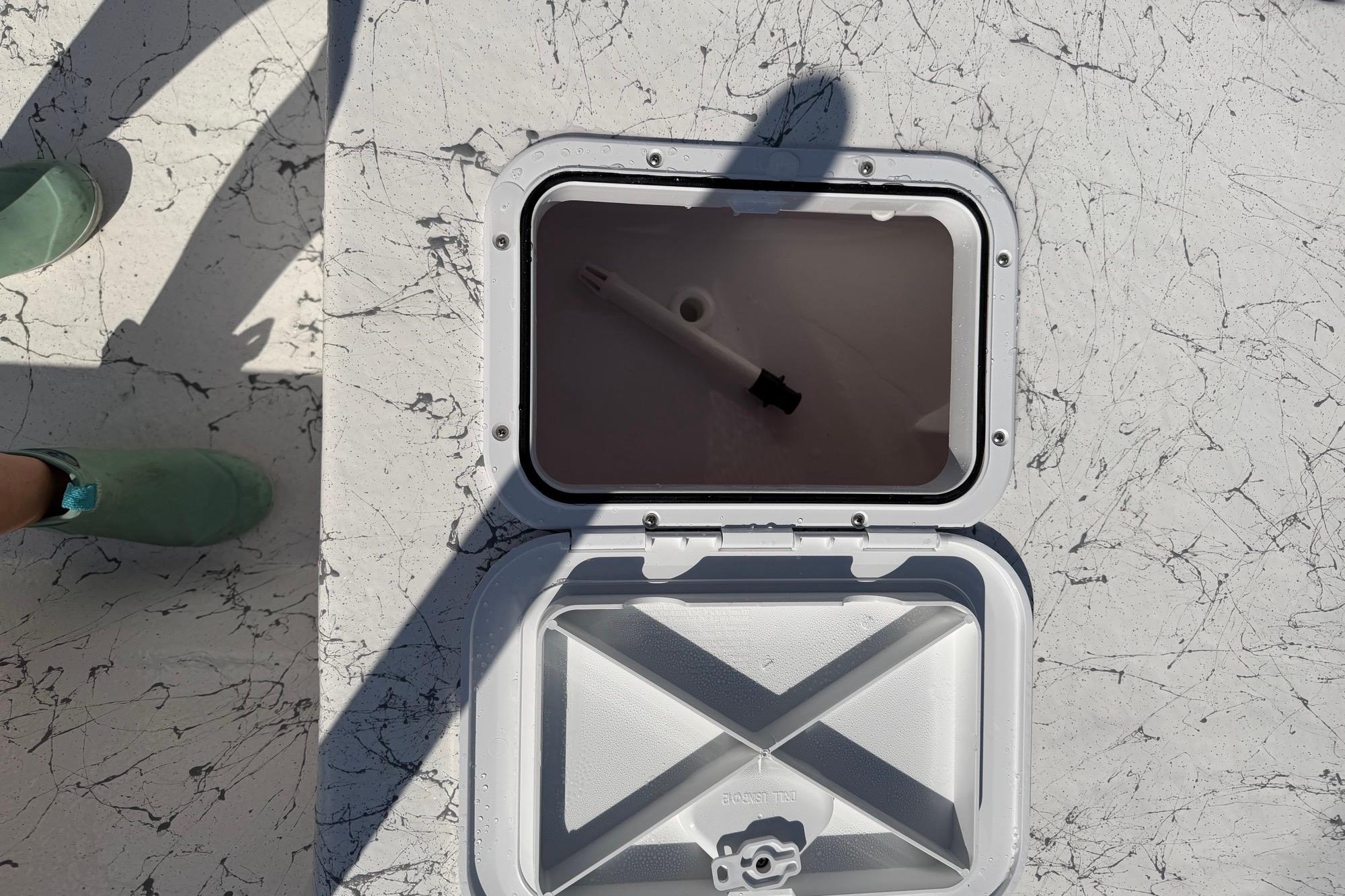 Open hatch on 2027 Coastal Skiff 184 boat deck with shadow and green shoes visible.