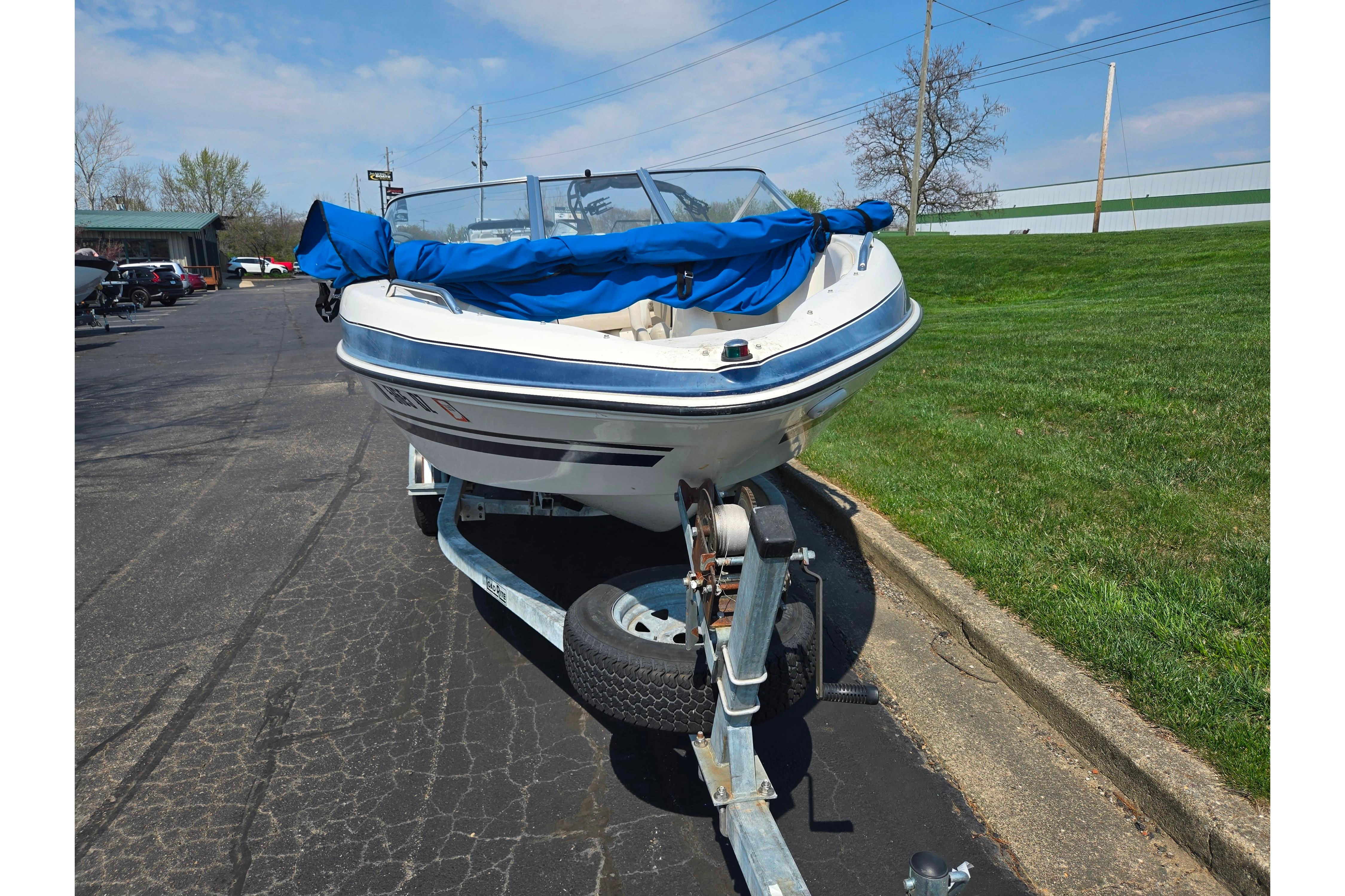 2007 Glastron GT 185 boat on trailer with blue cover, parked on asphalt.
