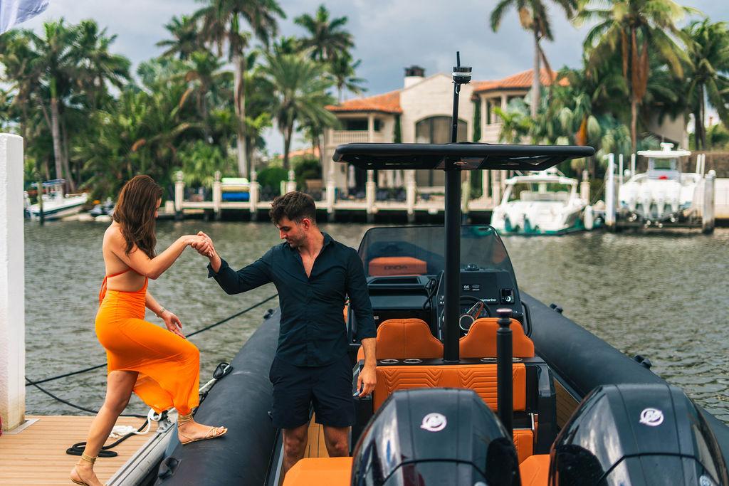 Couple boarding 2025 Onda Magna boat at a tropical marina, surrounded by palm trees.