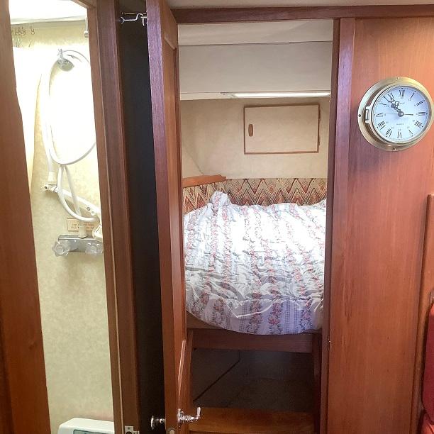 1982 Trojan F32 cabin interior with bed, clock, and wooden paneling.