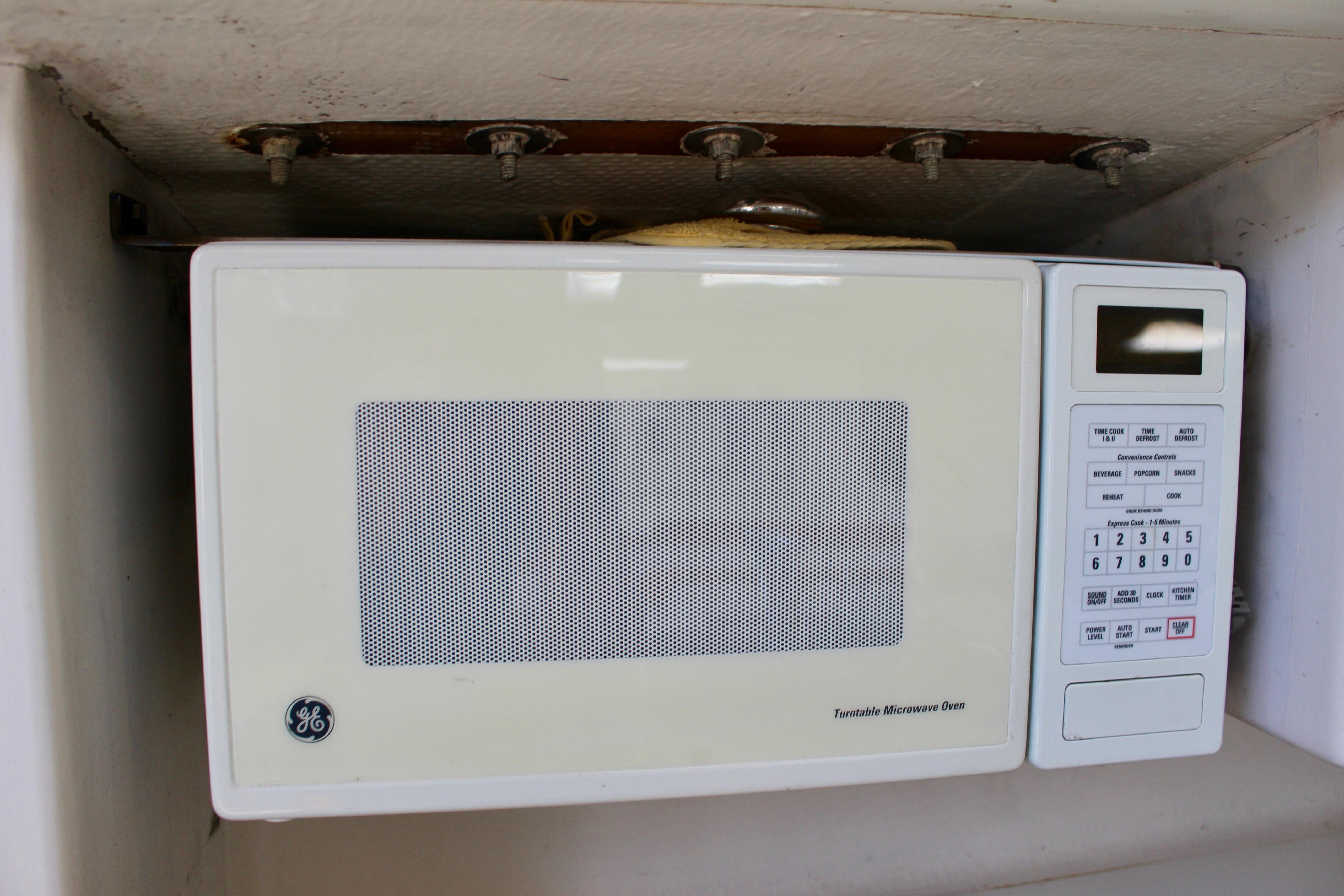 Old GE microwave oven with control panel, mounted under a shelf.
