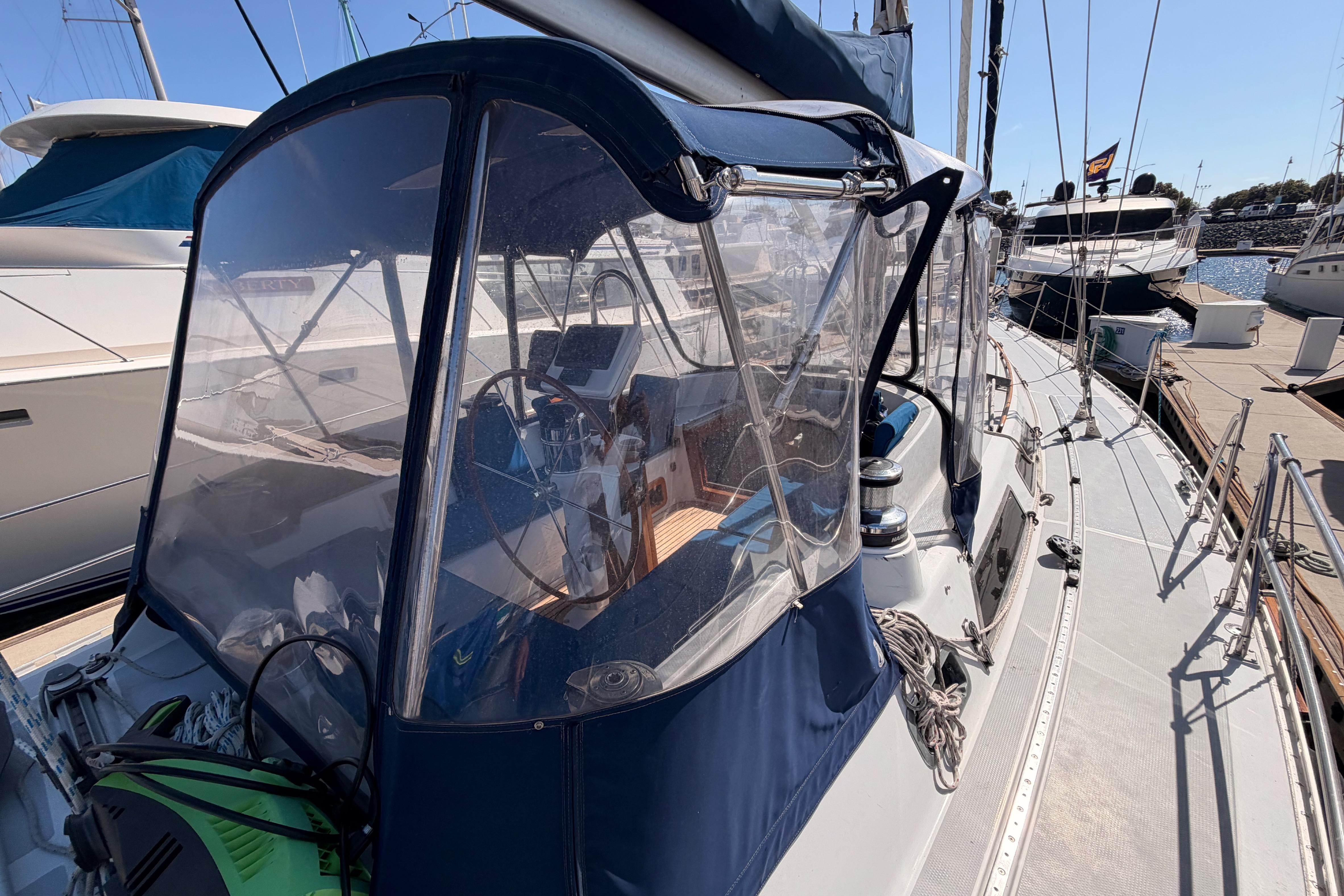 Sailboat cockpit of a 1991 Hylas 51, featuring a clear enclosure and marina view.
