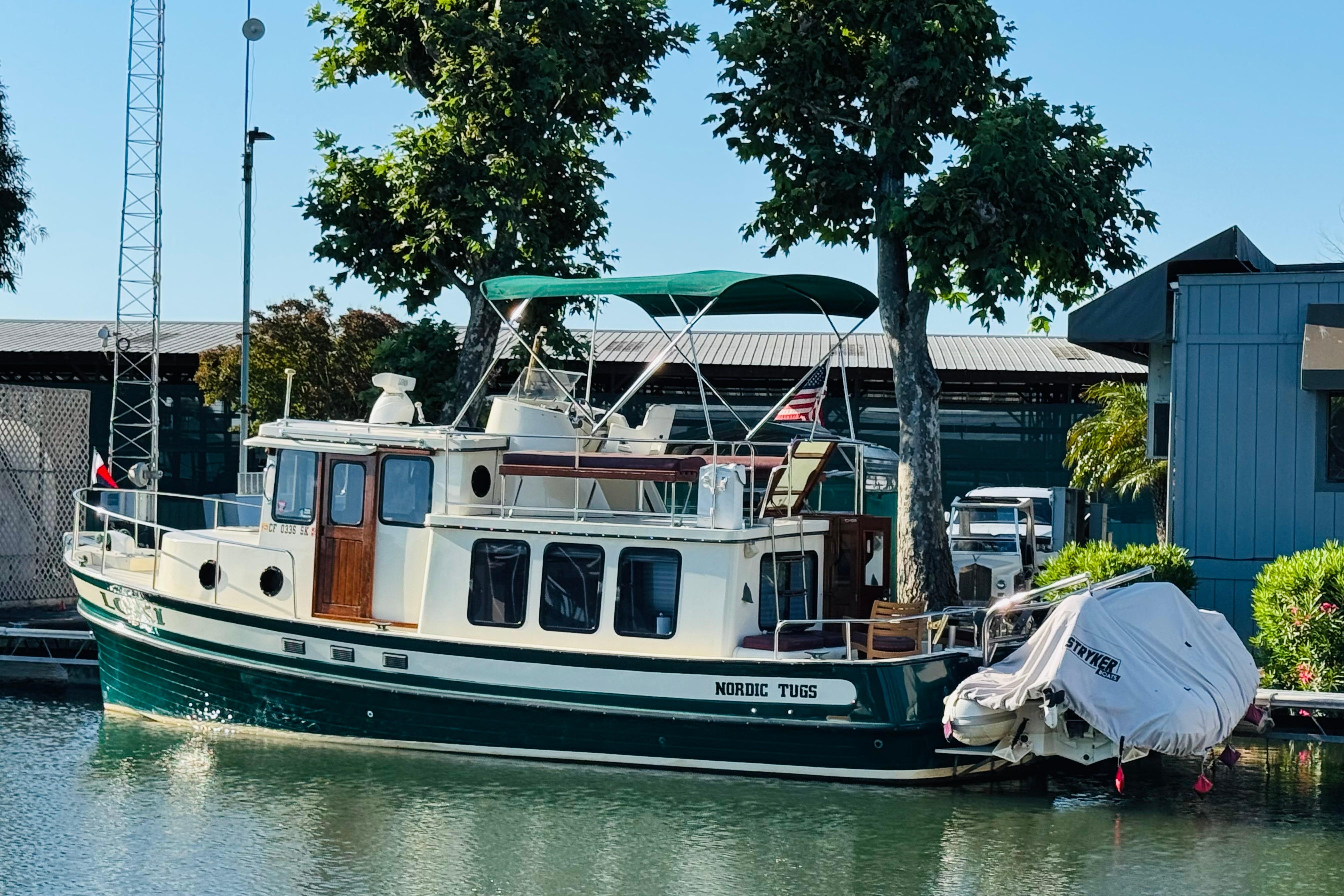 1996 Nordic Tug 32 docked by trees, featuring classic design and green canopy.
