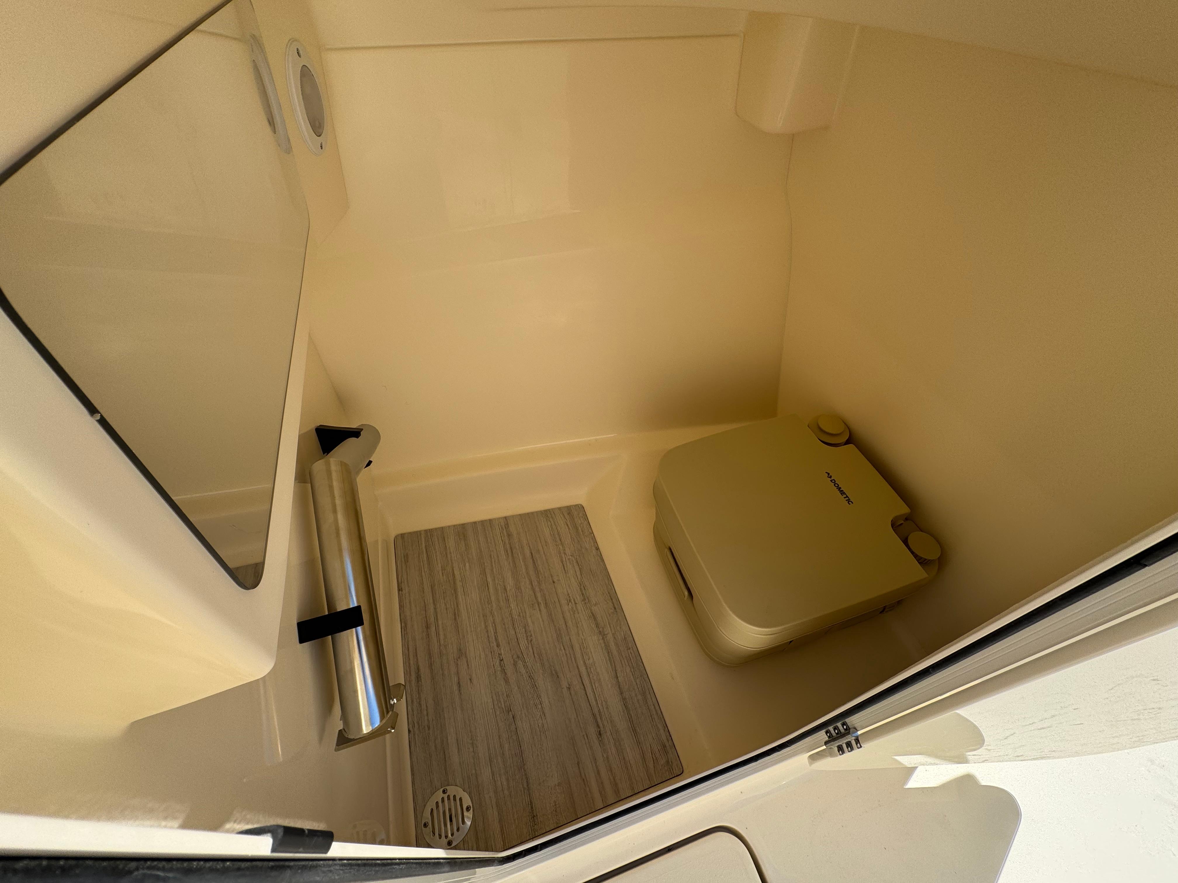 Interior of 2025 Scout 215 Dorado boat with compact toilet and wooden flooring.