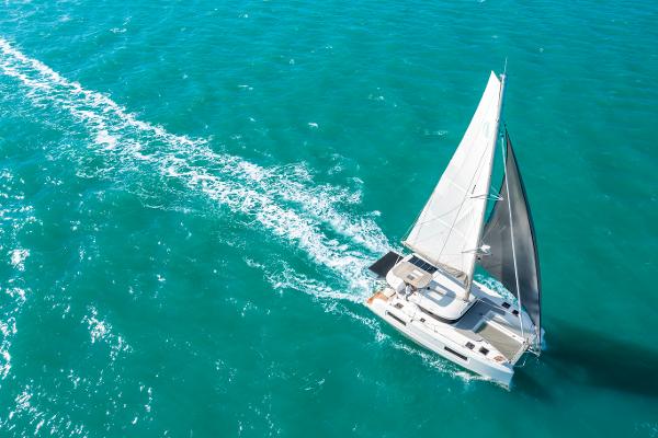 Aerial view of 2025 Lagoon 38 sailing on turquoise ocean waters.
