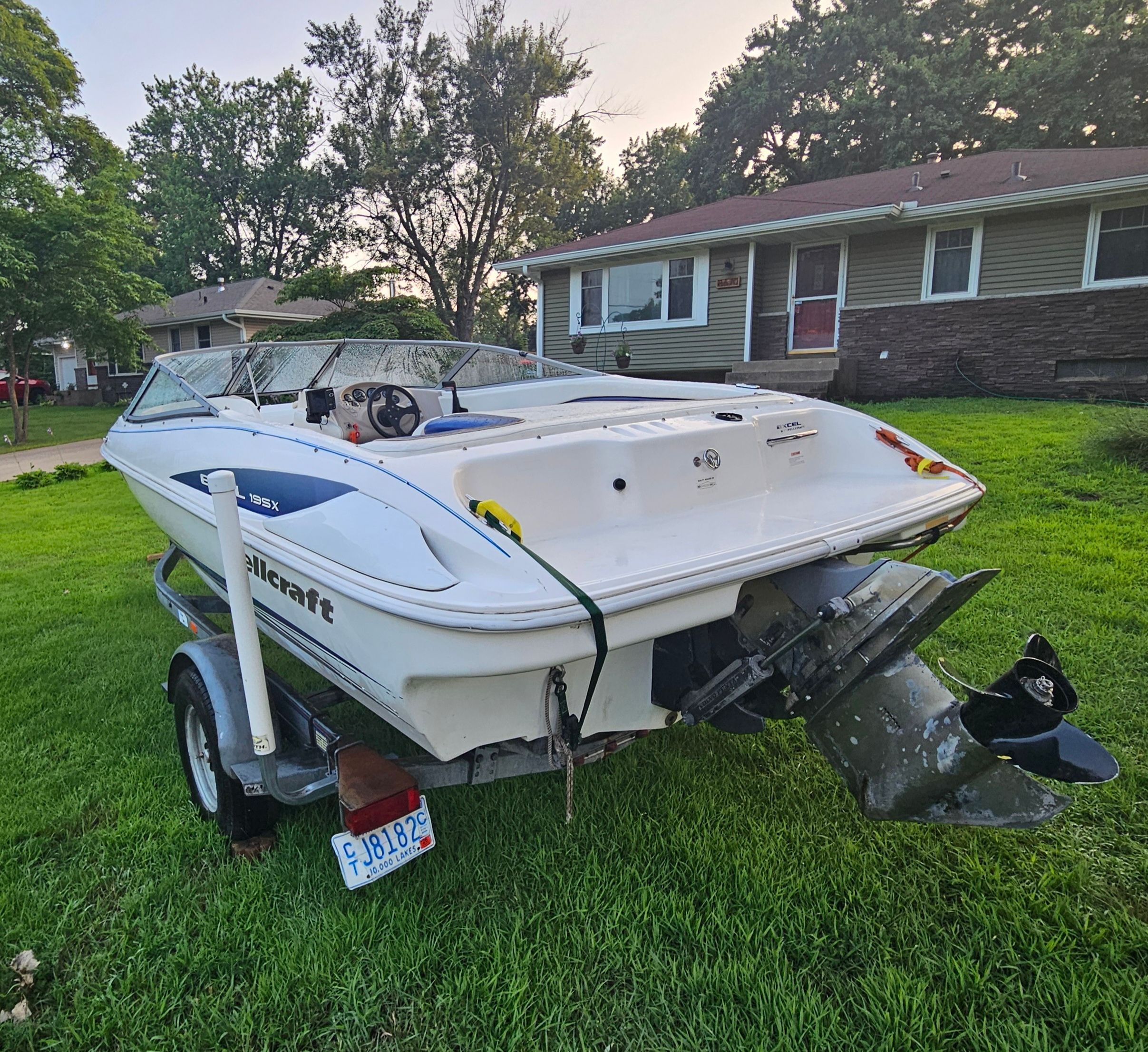 A 1996 Wellcraft Excel boat on a trailer in a front yard.