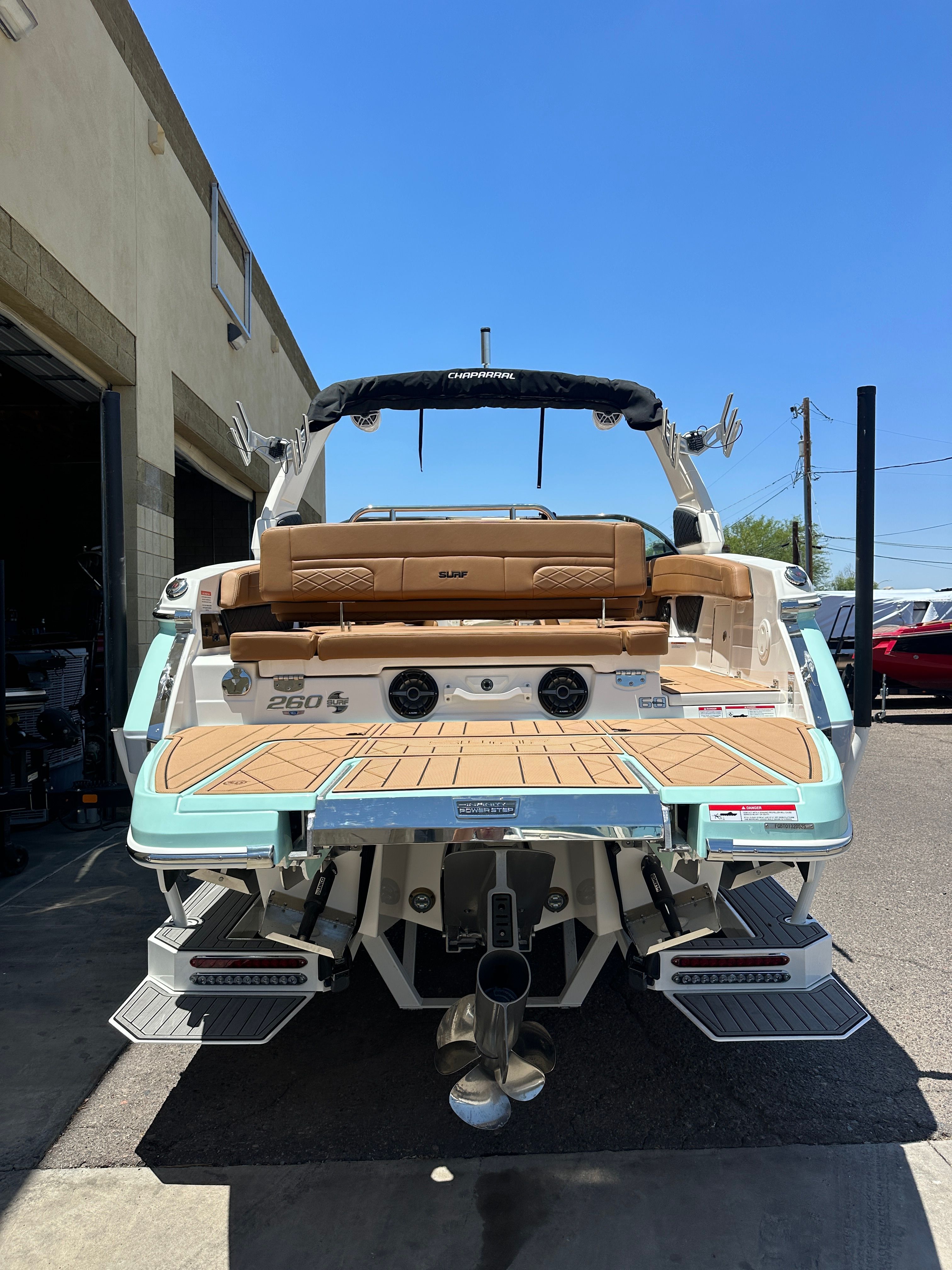 The image shows a 2025 Chaparral 26 Surf boat in a garage. It features a modern design with a spacious deck and comfortable seating.
