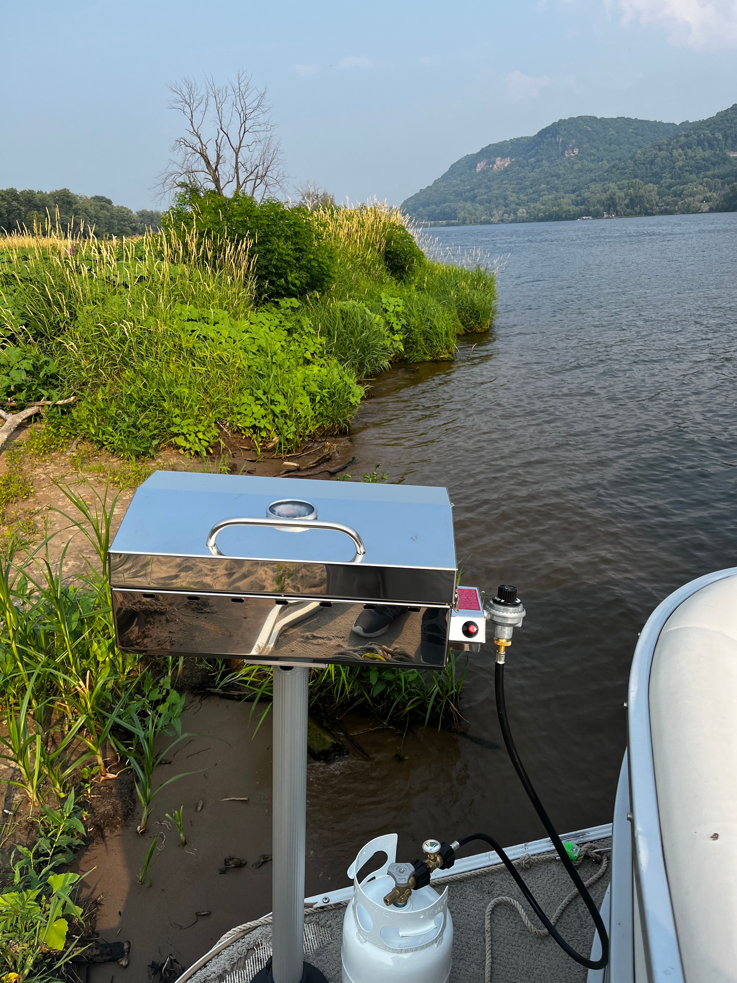 A grill on a boat overlooking a river and green banks.