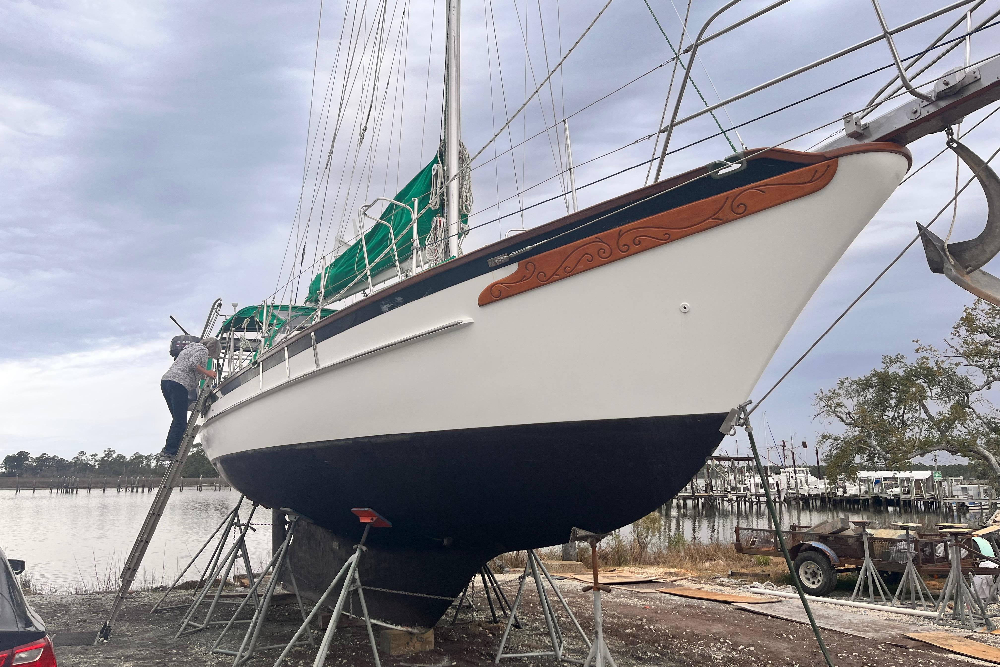 1989 Cabo Rico 34 sailboat on stands, with person climbing ladder, near waterfront.