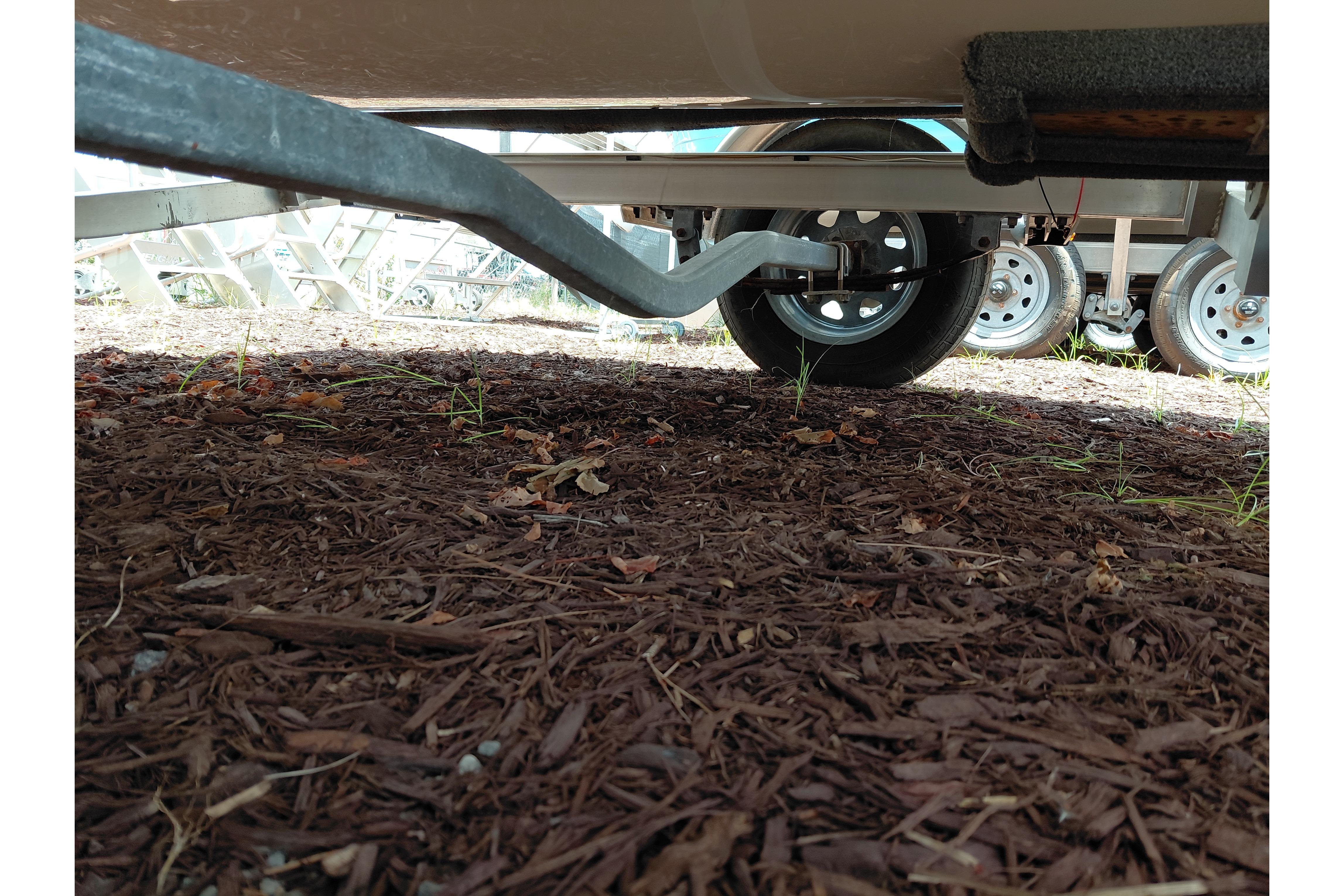 Underneath view of a 2023 Key West 189 FS boat trailer on mulch ground.