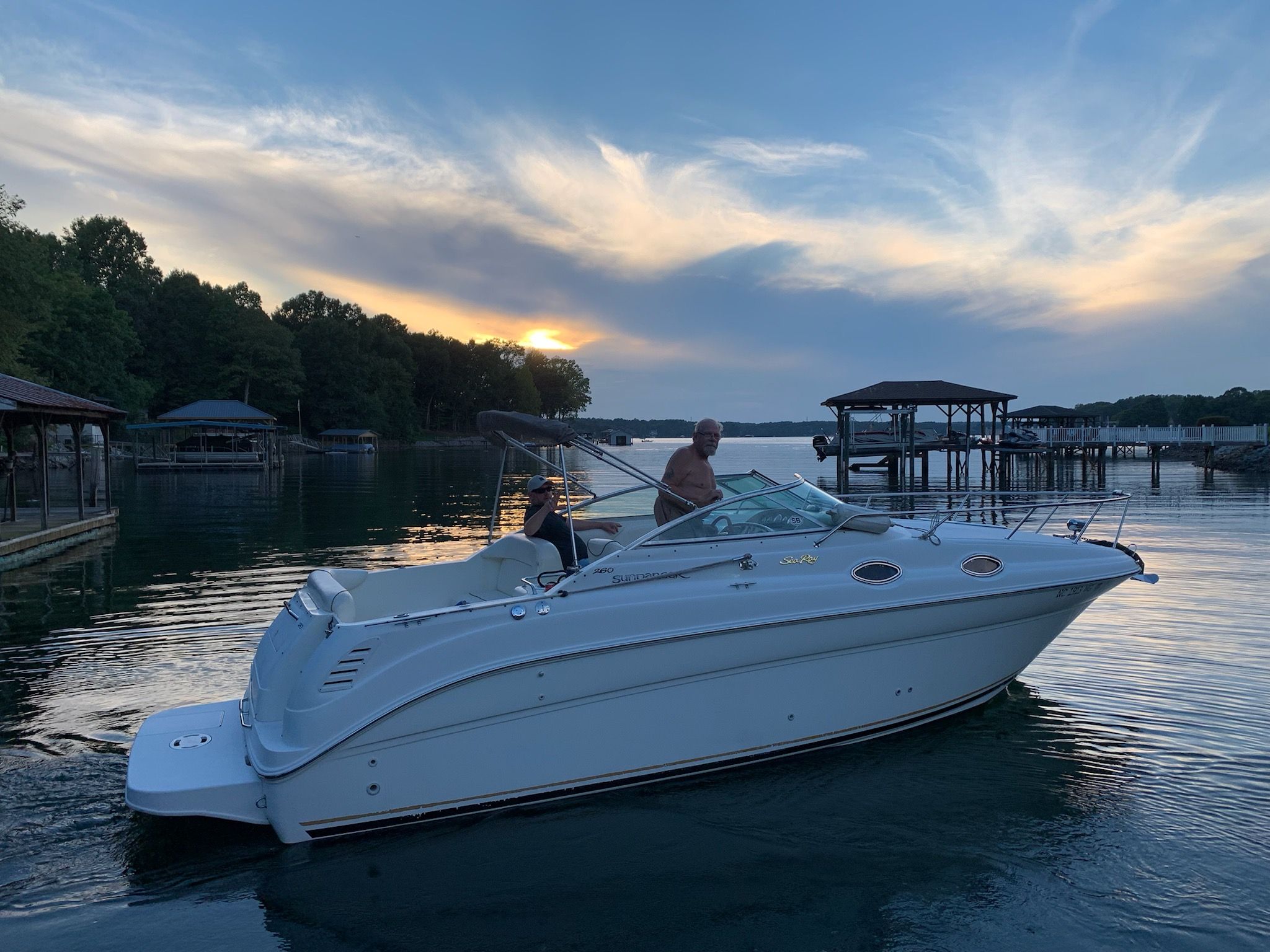 A white motorboat cruises on a calm lake at sunset.