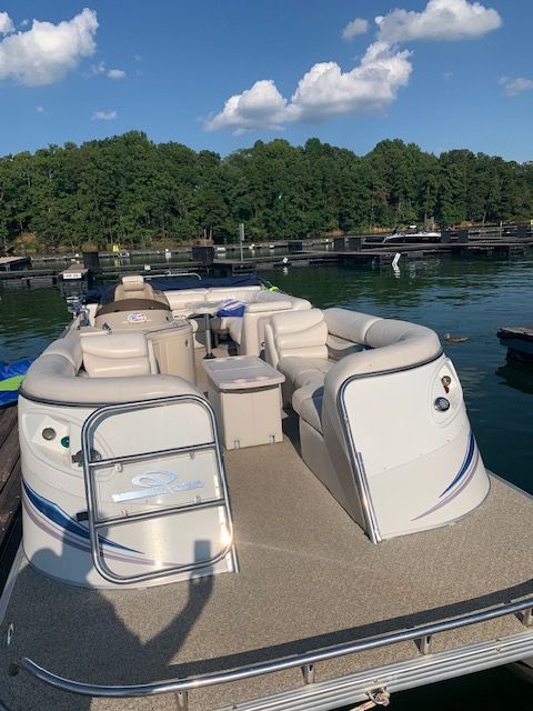 A pontoon boat is docked on a calm lake with a wooded shoreline in the background.