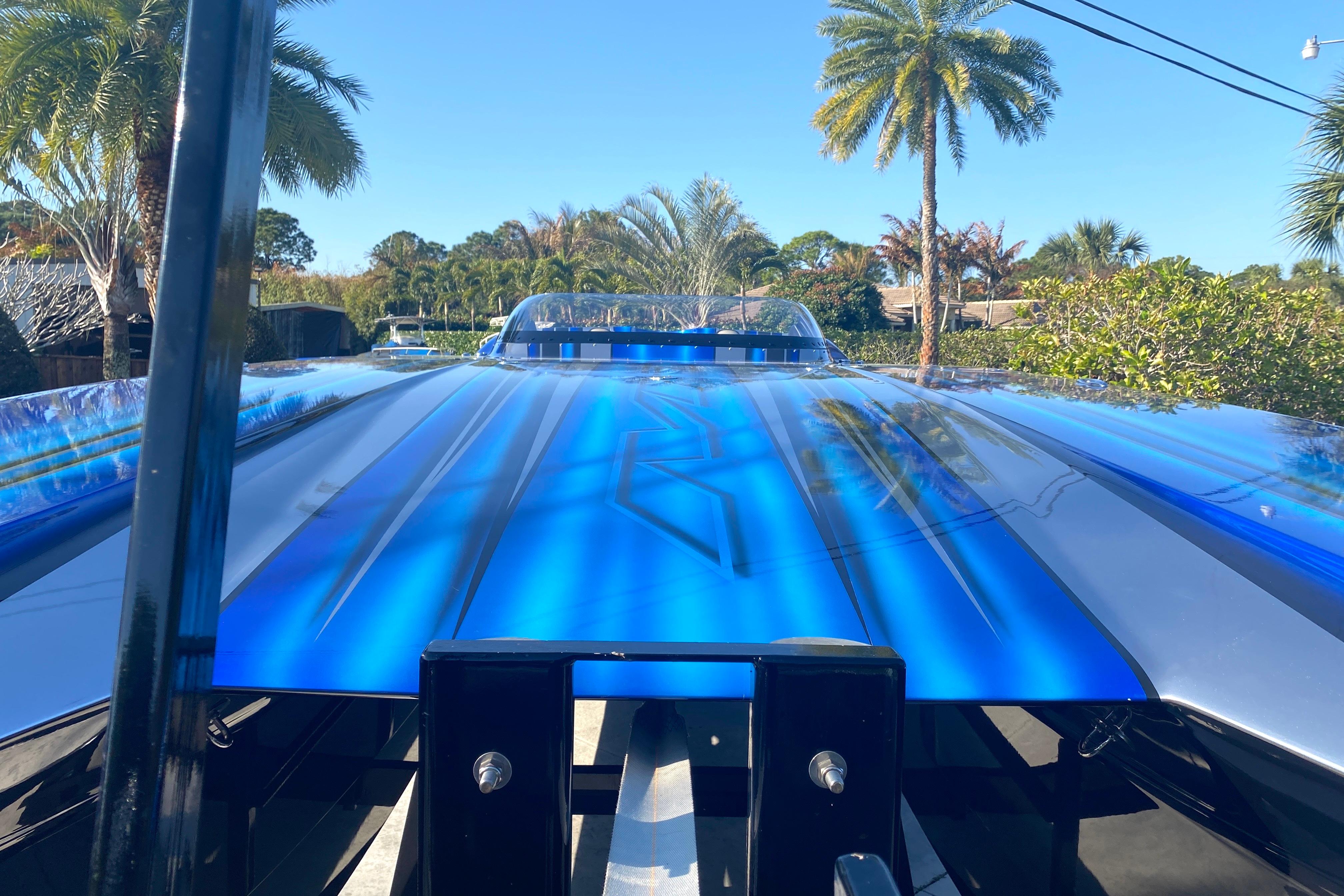 Blue MTI 44 RP speedboat with sleek design, surrounded by palm trees, under clear blue sky.