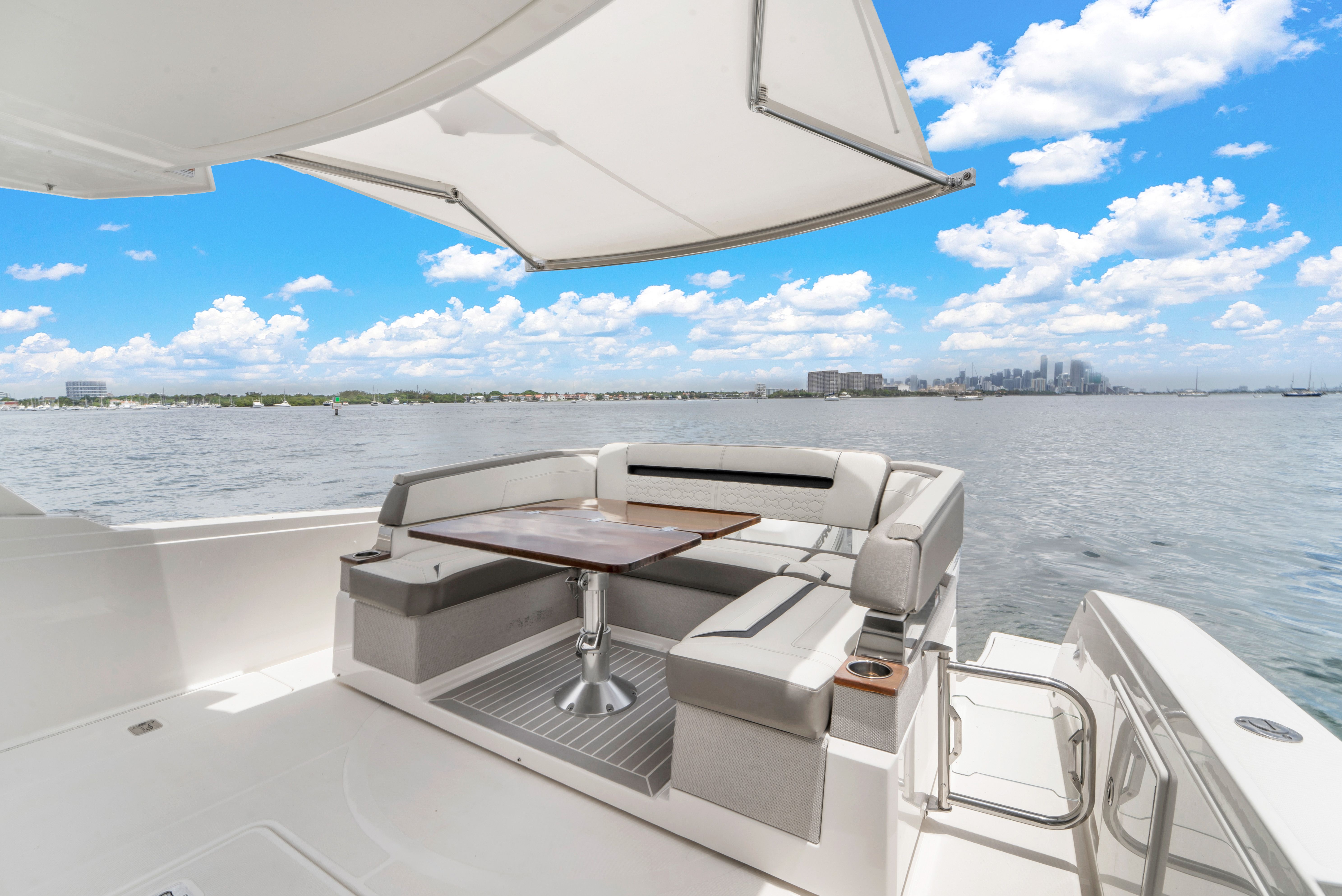 The image shows the stern of a Tiara Yachts 38 LS with seating and a table. Water and a city are visible in the background.