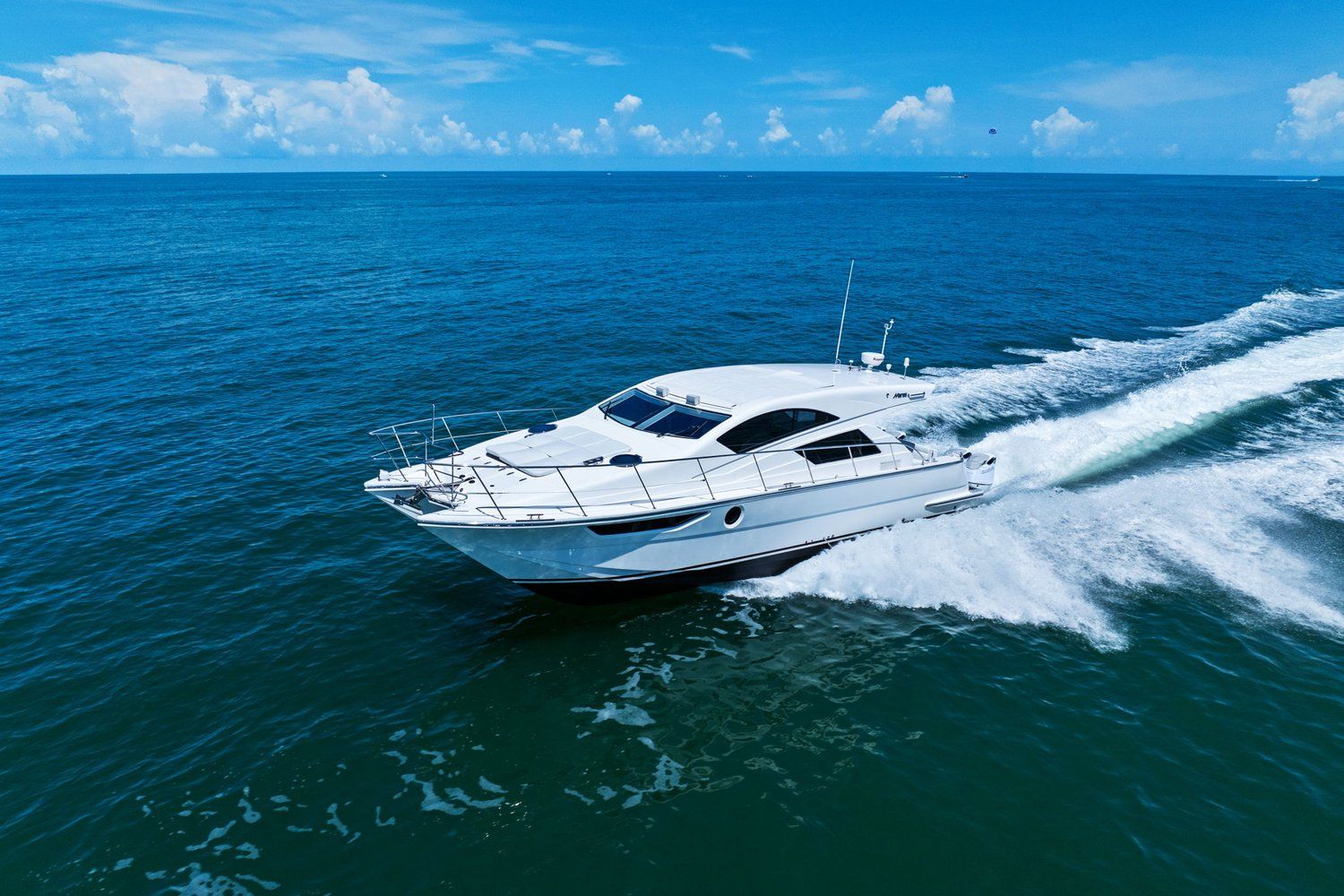 A white catamaran speeds across the blue sea under a clear sky.