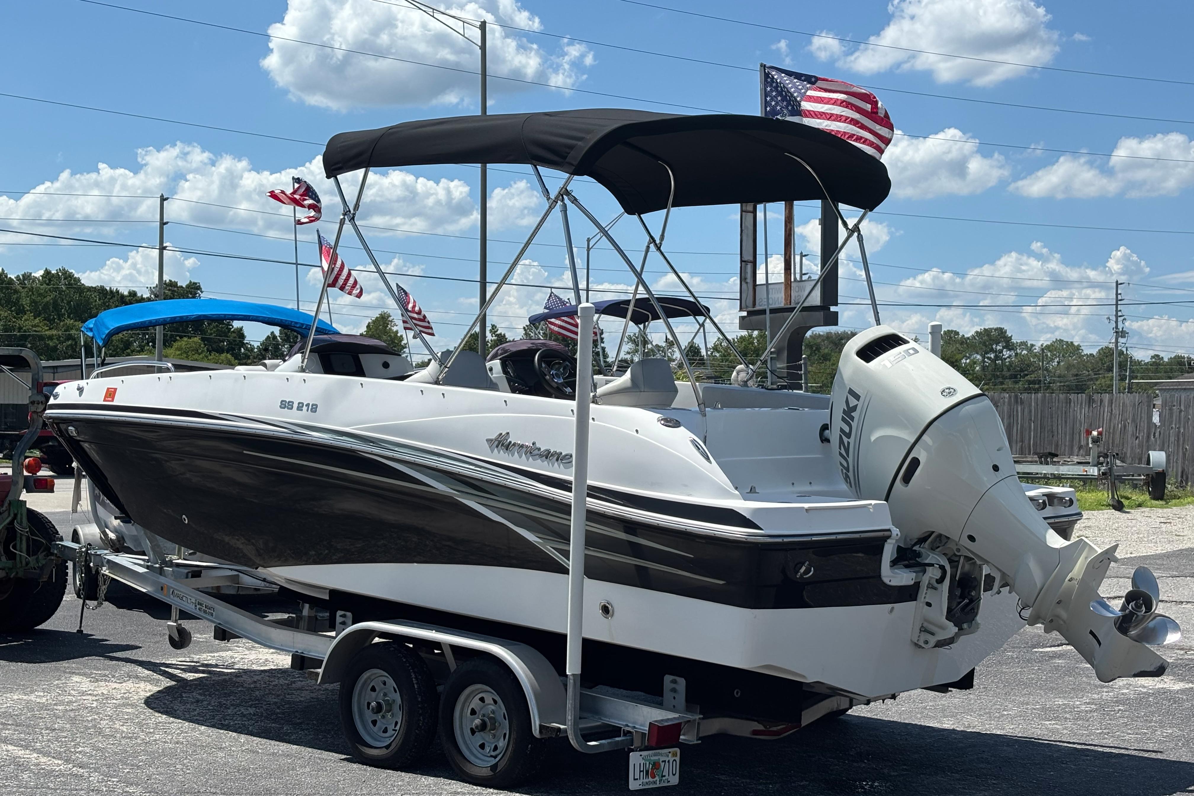 2019 Hurricane Sundeck Sport 218 OB boat on trailer, flags waving, sunny day.