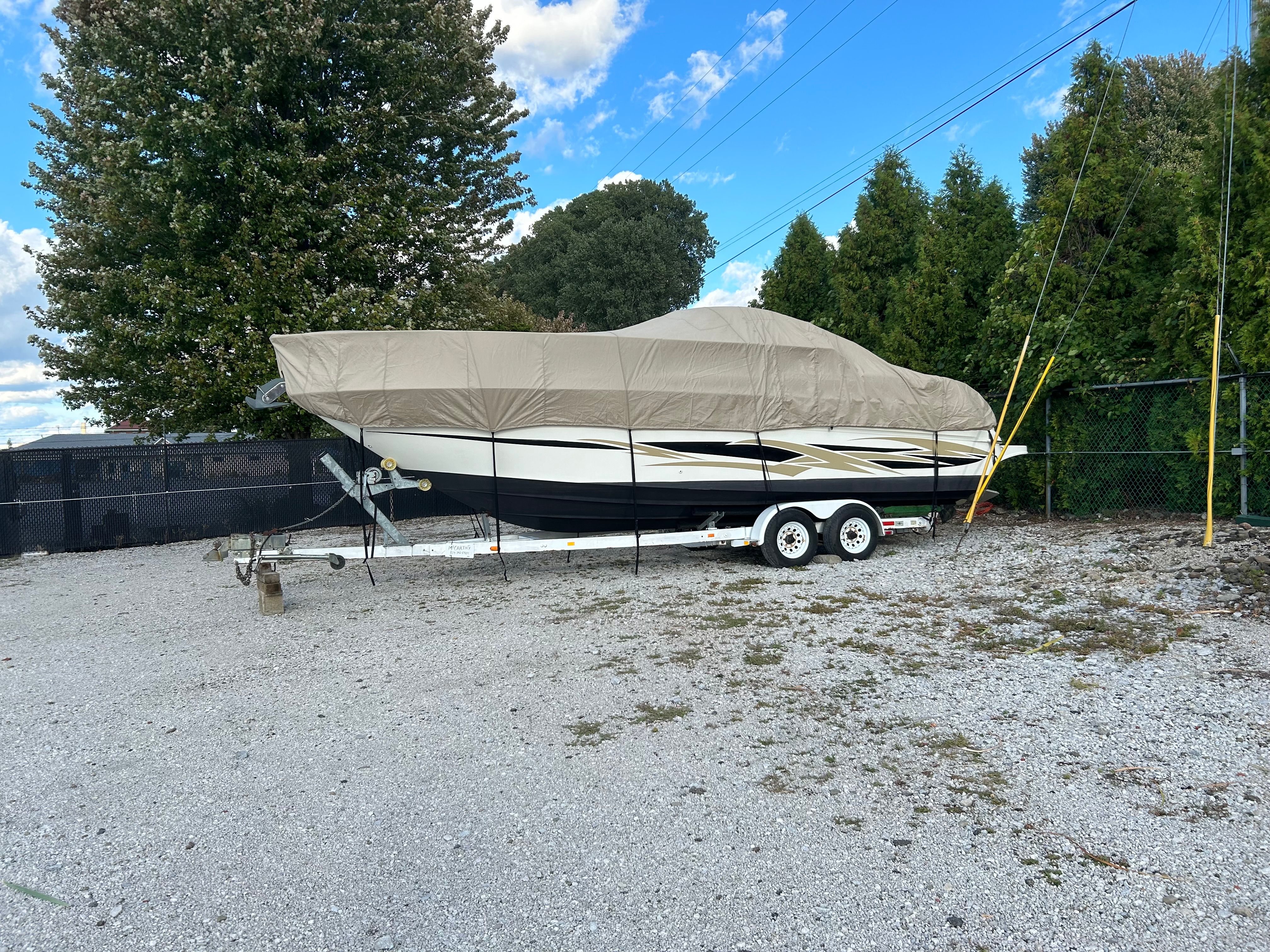 A 1998 Sea Ray 270 Sundancer on a trailer, covered, in a gravel lot.
