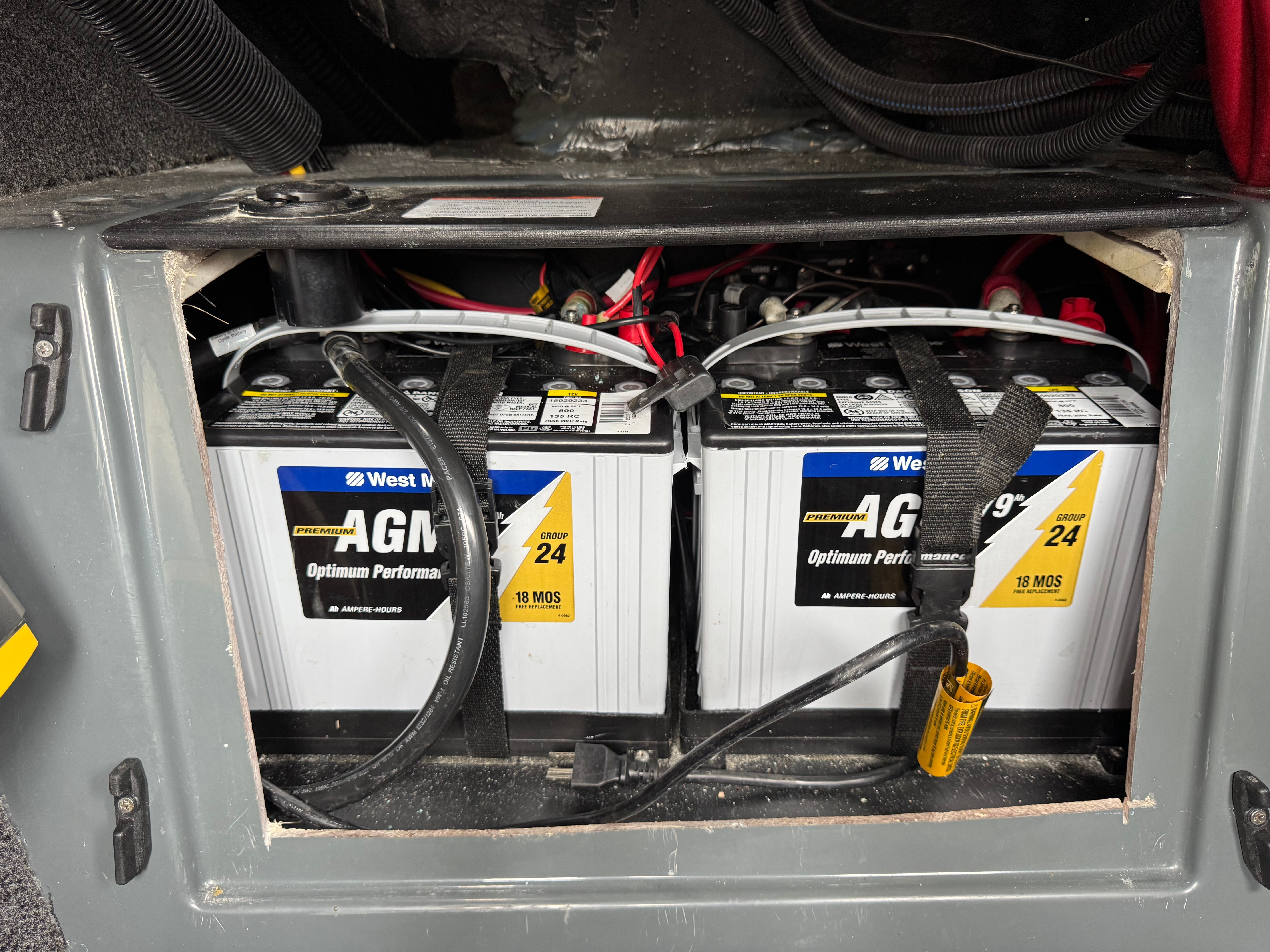 Two AGM batteries are installed in a boat, surrounded by cables and straps.