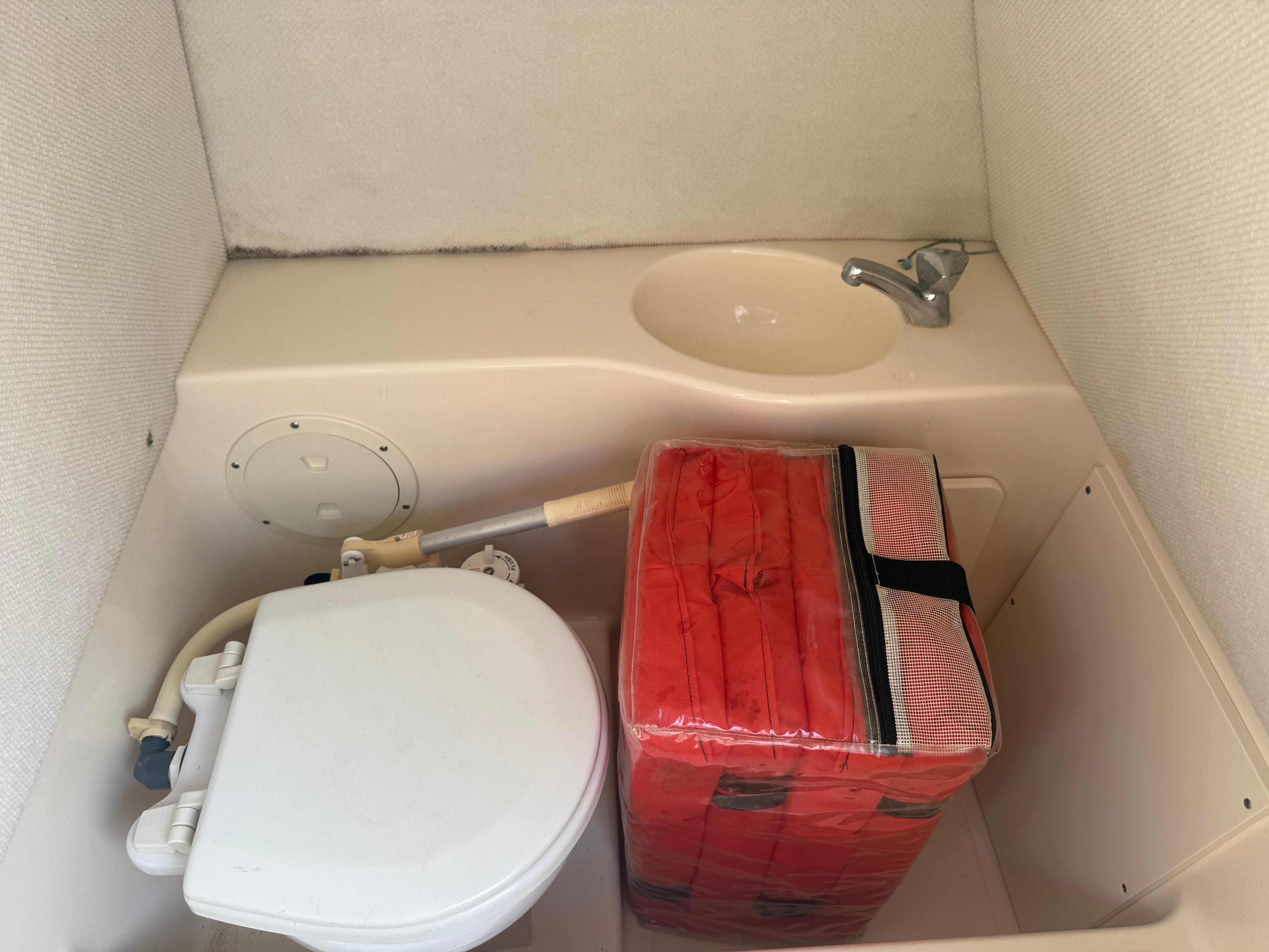 Compact boat bathroom with toilet, sink, and red life jacket storage on a 2002 Pursuit 2470 CC.