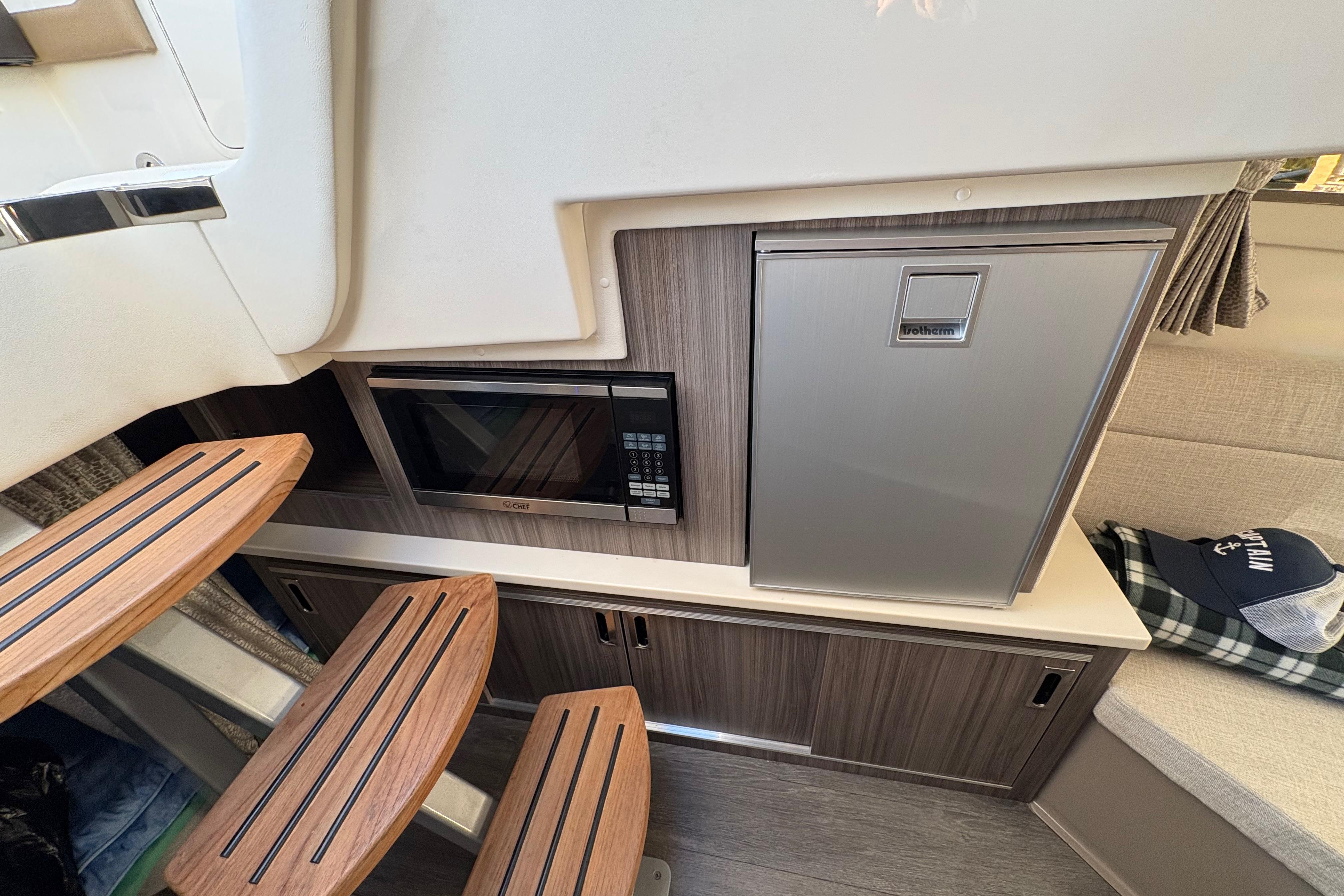 Interior of 2022 Sea Ray Sundancer 320 with microwave, fridge, and wooden steps.
