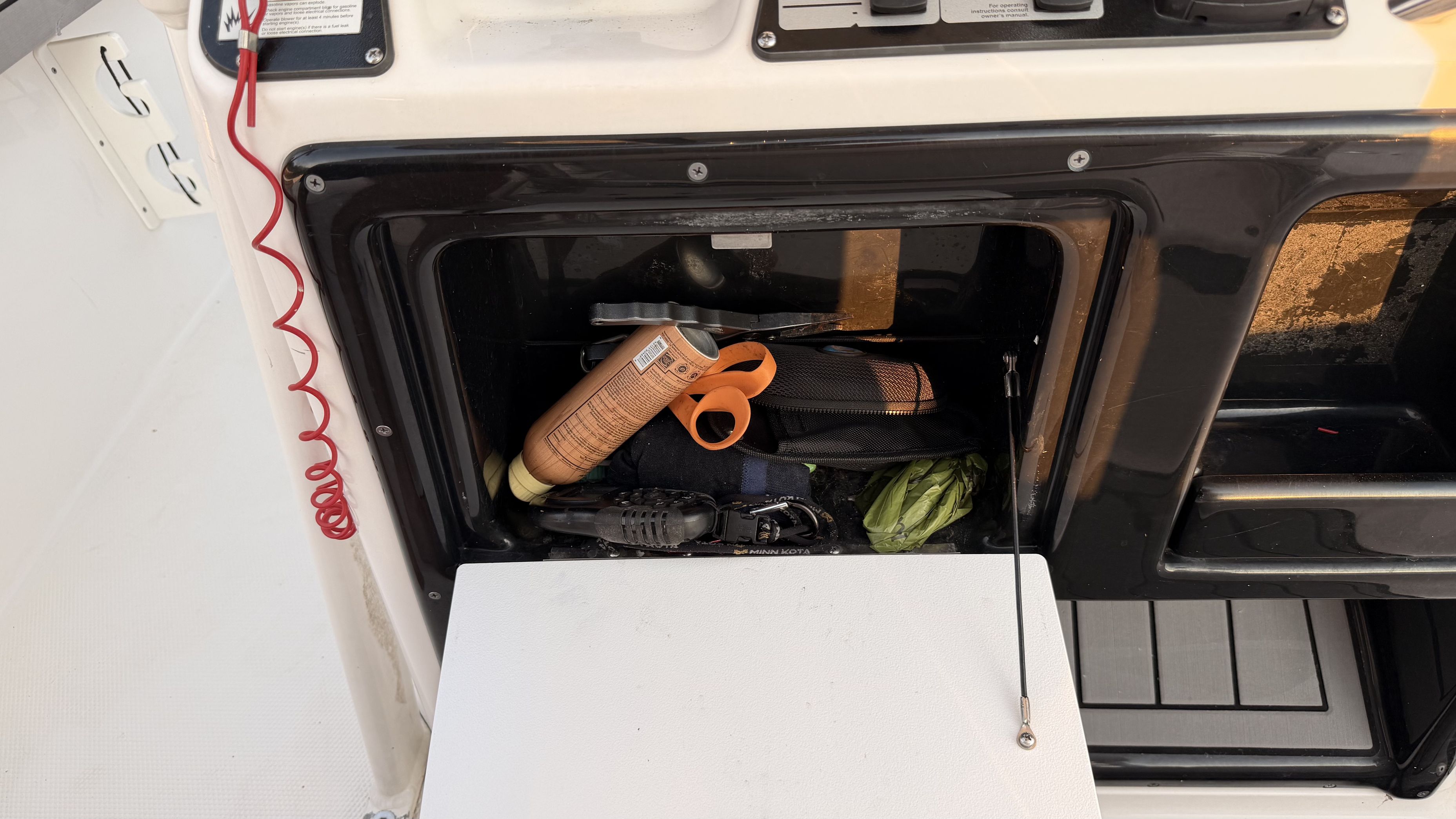 An open storage compartment on a boat with various items like sunscreen and tools.