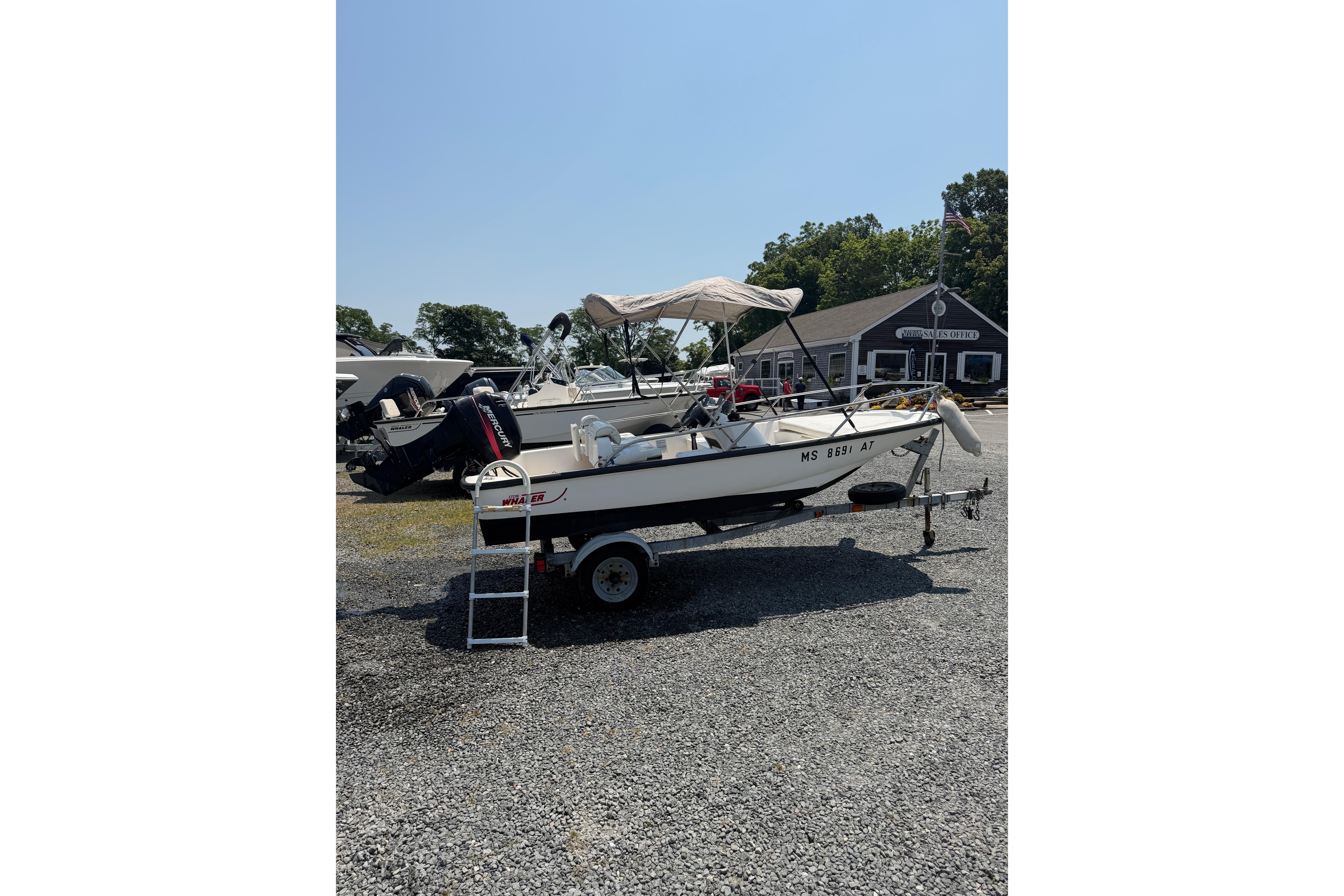 2003 Boston Whaler 130 Super Sport boat on trailer, parked outdoors on gravel.