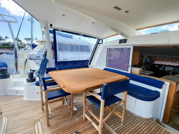 2009 Catana 65 yacht interior with wooden dining table and blue cushioned seating.