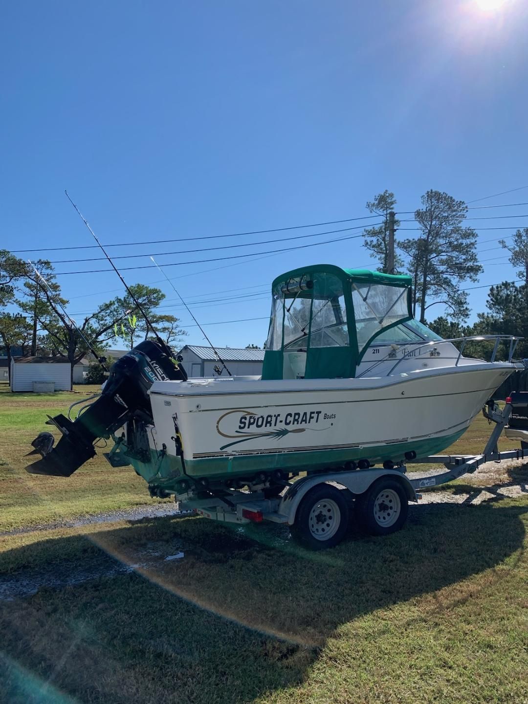 A 1998 Sport-Craft 211WAC boat on a trailer outdoors, surrounded by trees.