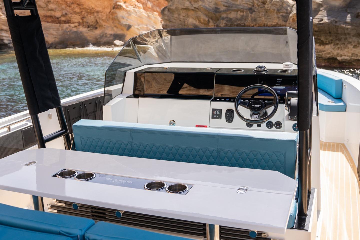 2026 De Antonio Yachts D29 interior with modern helm and seating, docked by rocky shore.