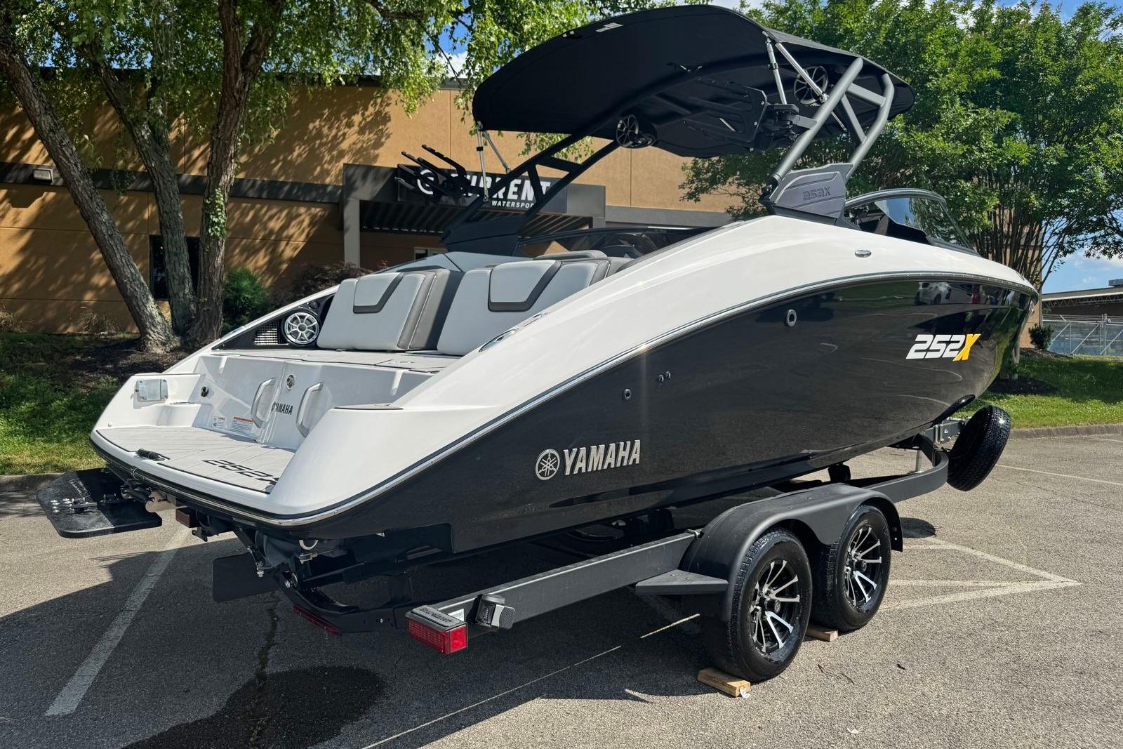 2023 Yamaha Boats 252XE on trailer, sleek design, parked outdoors under trees.