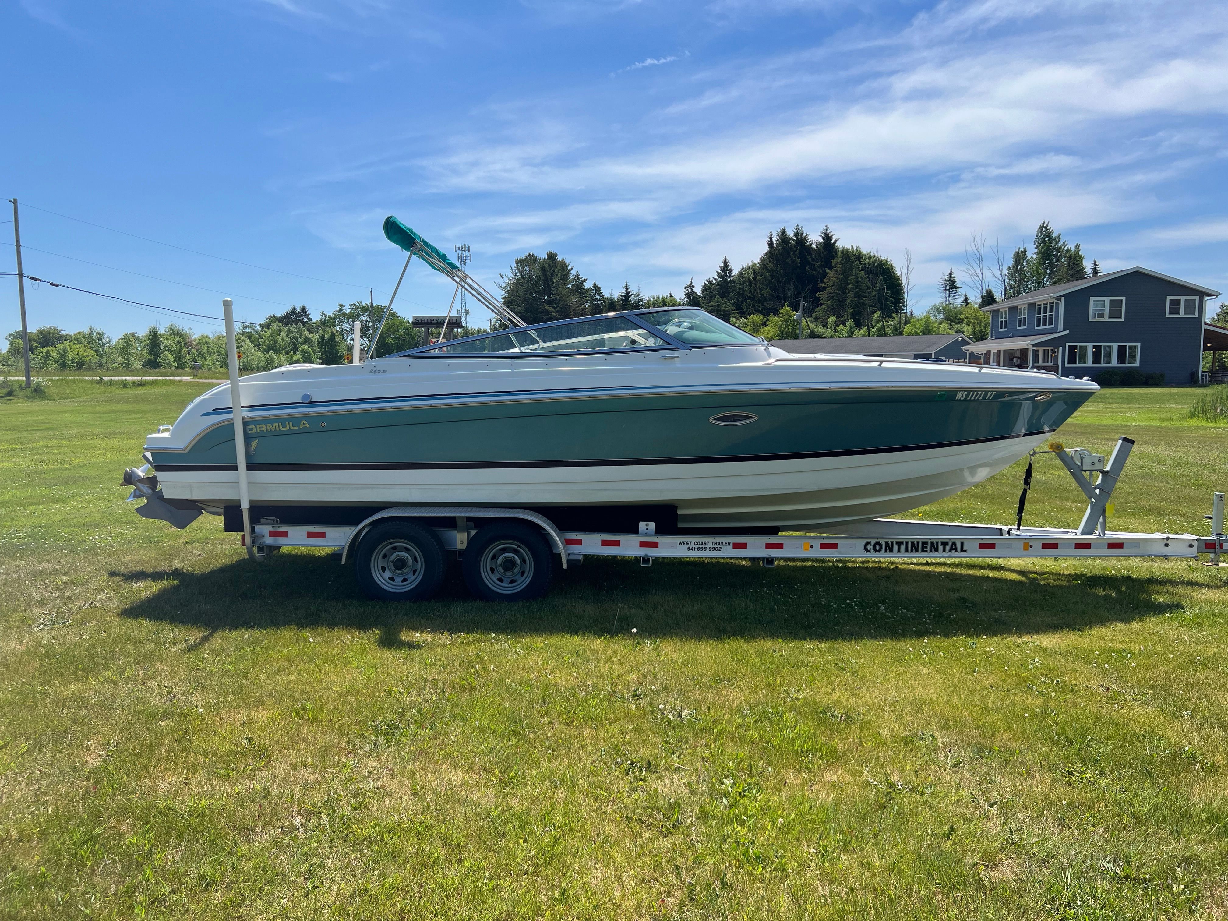 A 2005 Formula 260 Sun Sport boat on a trailer, parked on a grassy field.