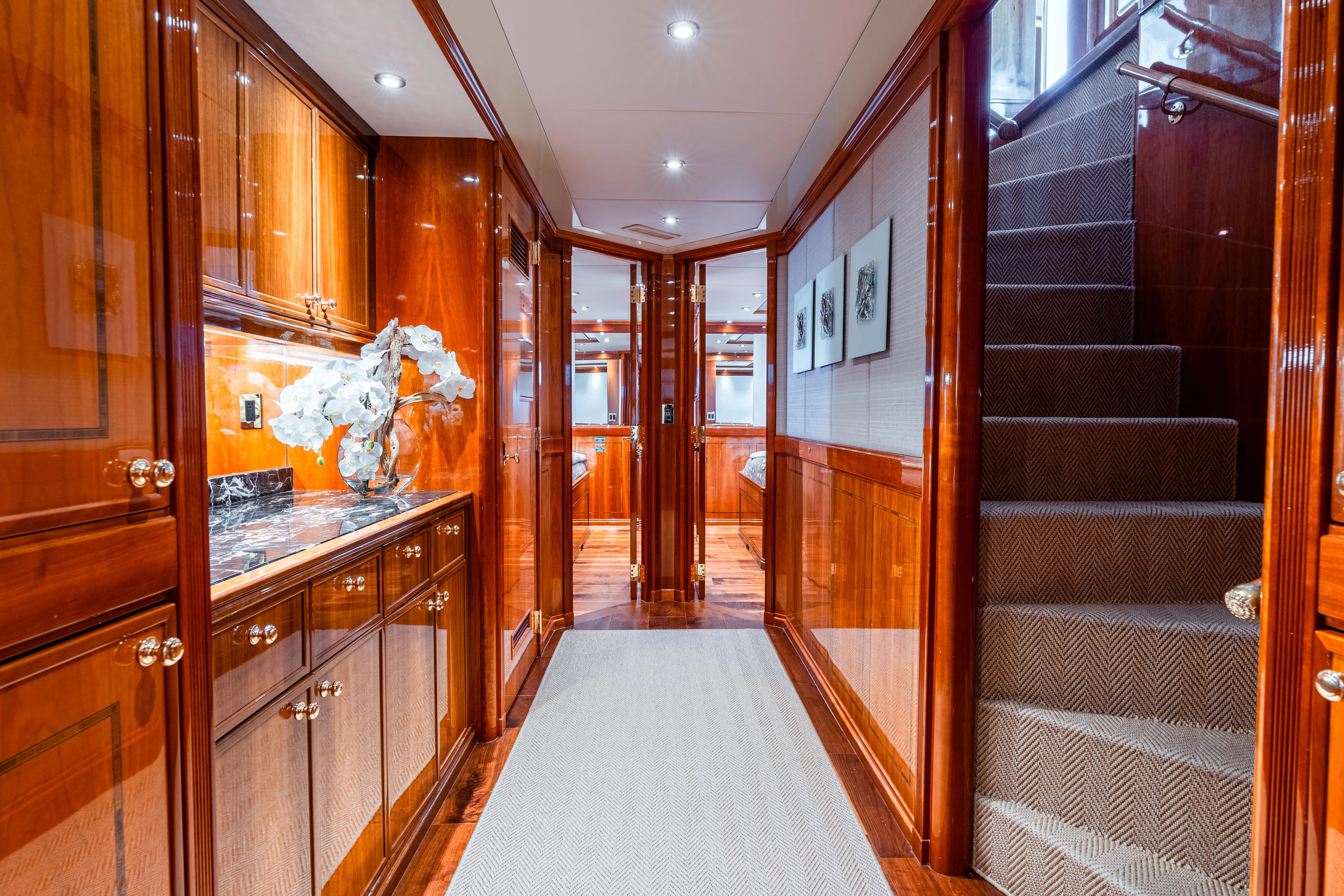 Luxurious yacht interior with glossy wood walls, carpeted floor, and staircase.