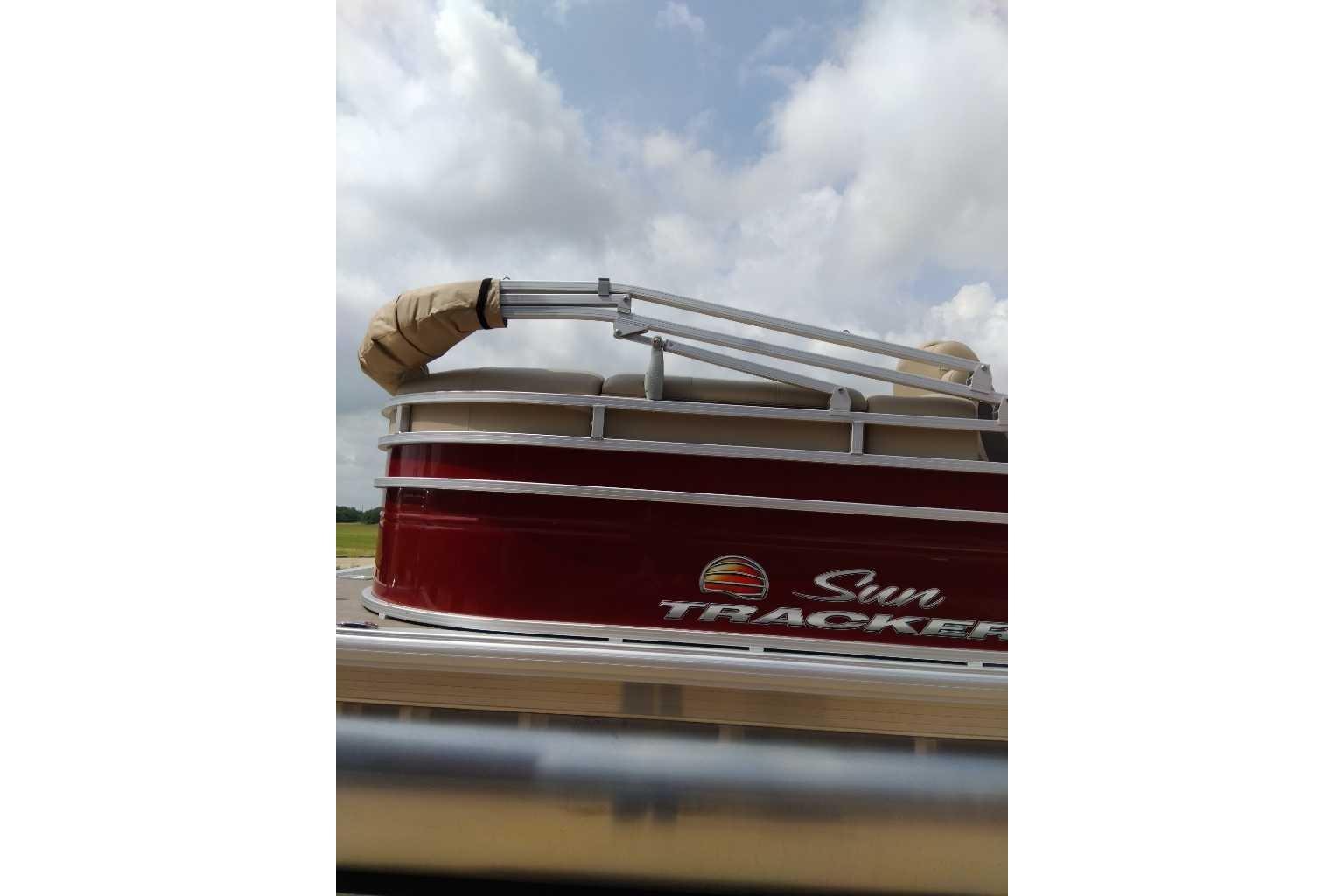 2025 Sun Tracker Party Barge 22 DLX pontoon boat with red exterior under cloudy sky.