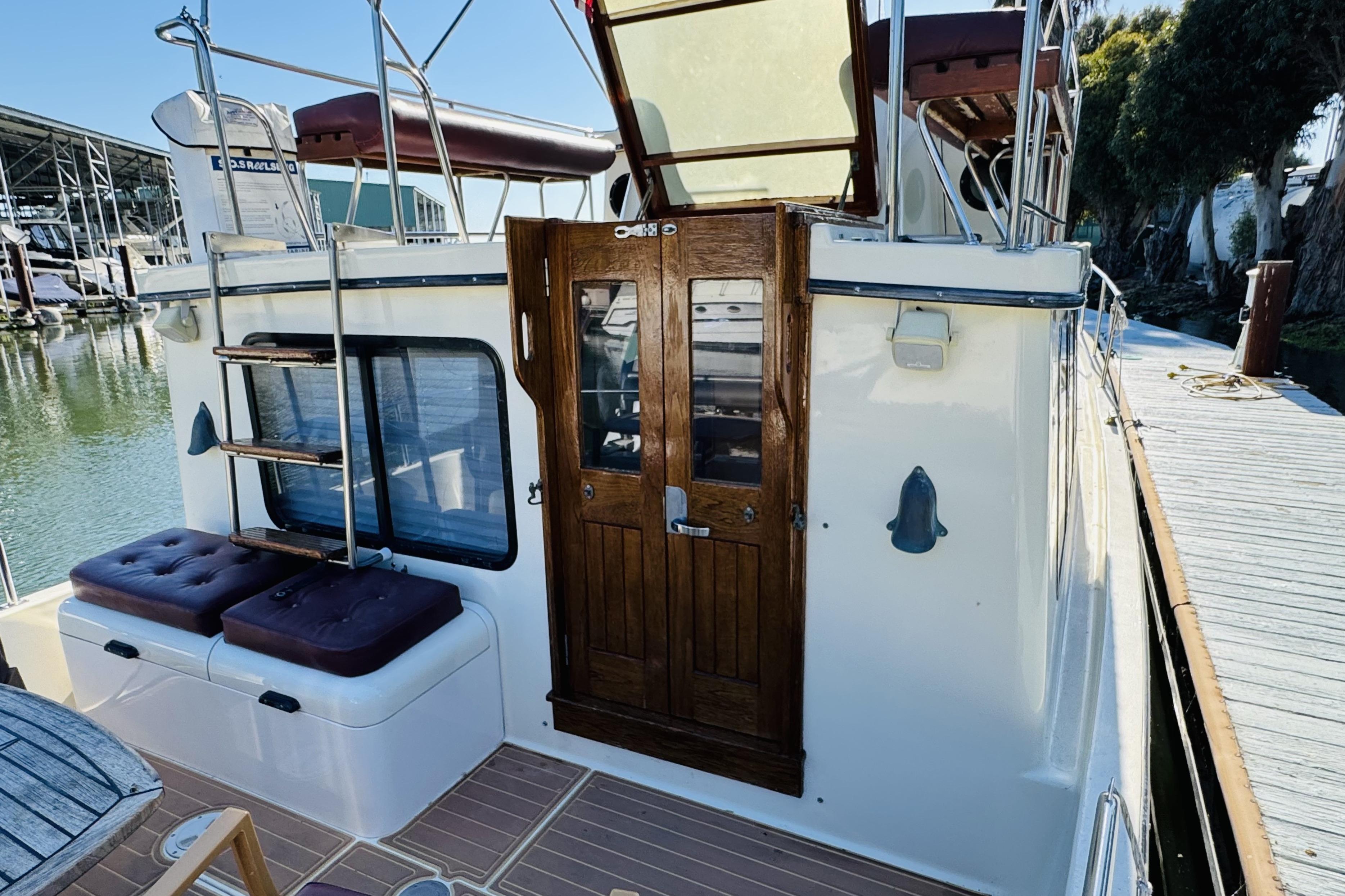 1996 Nordic Tug 32 docked, featuring wooden door, ladder, and cushioned seating on deck.