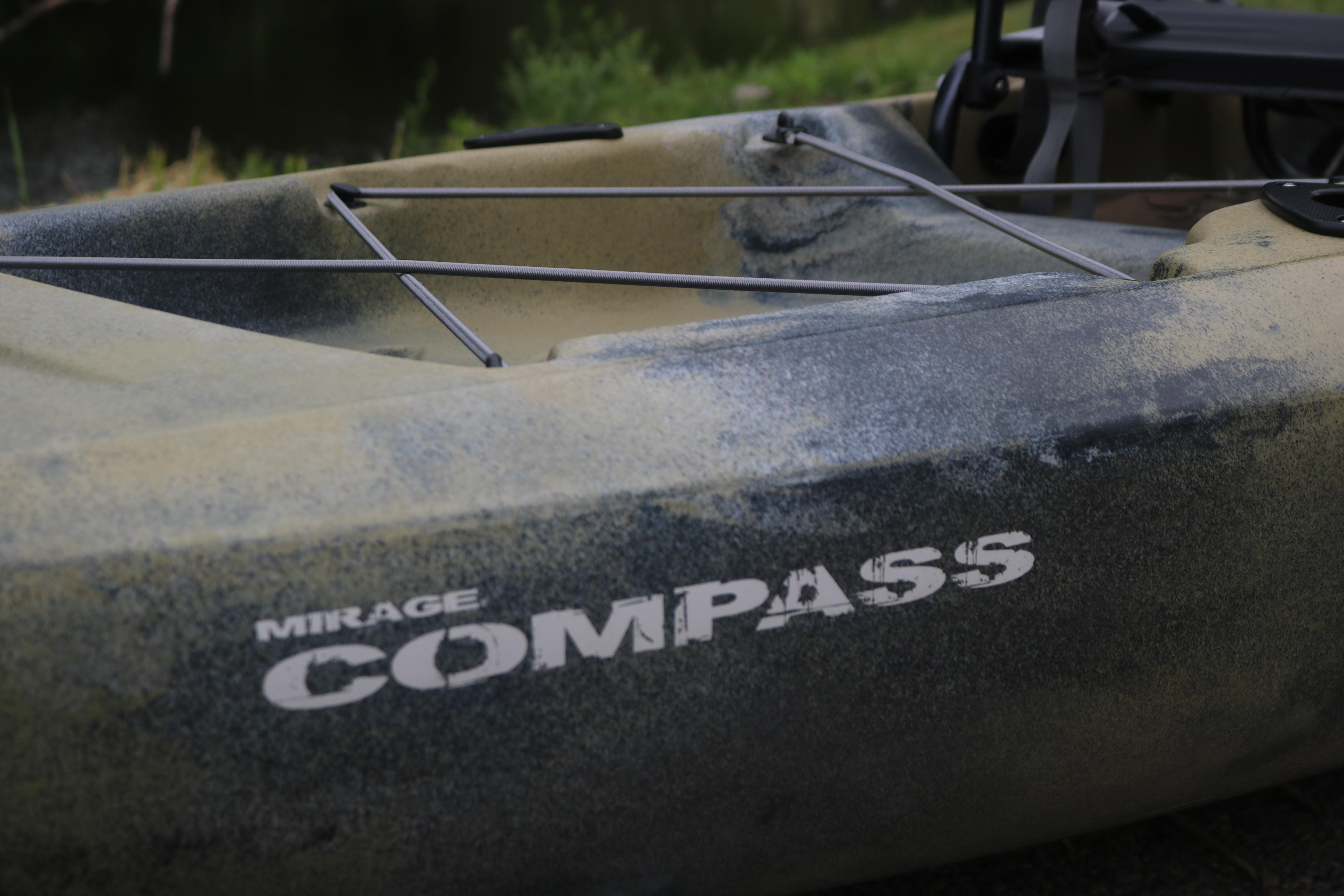 2023 Hobie Mirage Compass kayak with camouflage design near a serene water body.