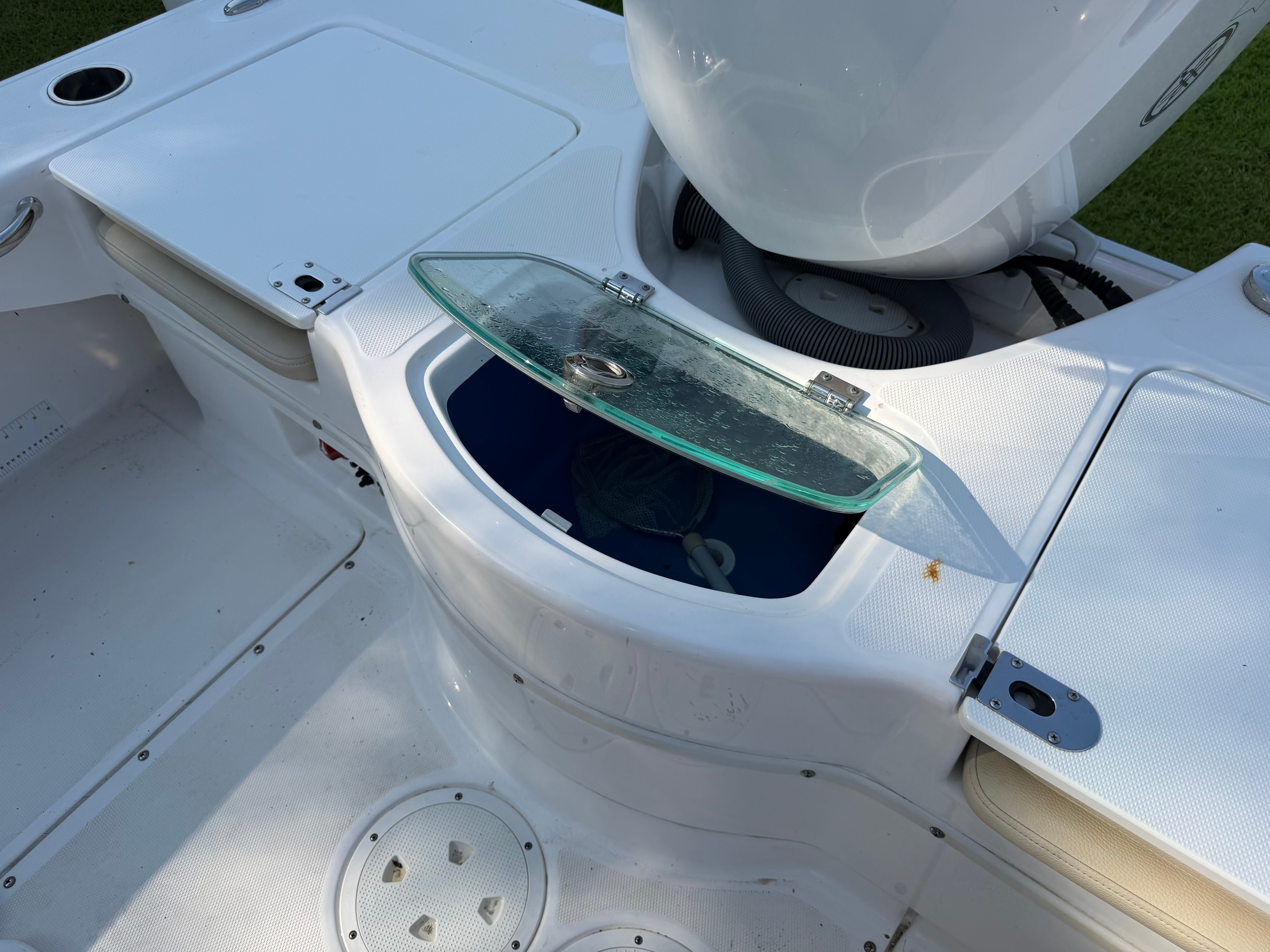 An open storage compartment on a white boat with a glass lid.