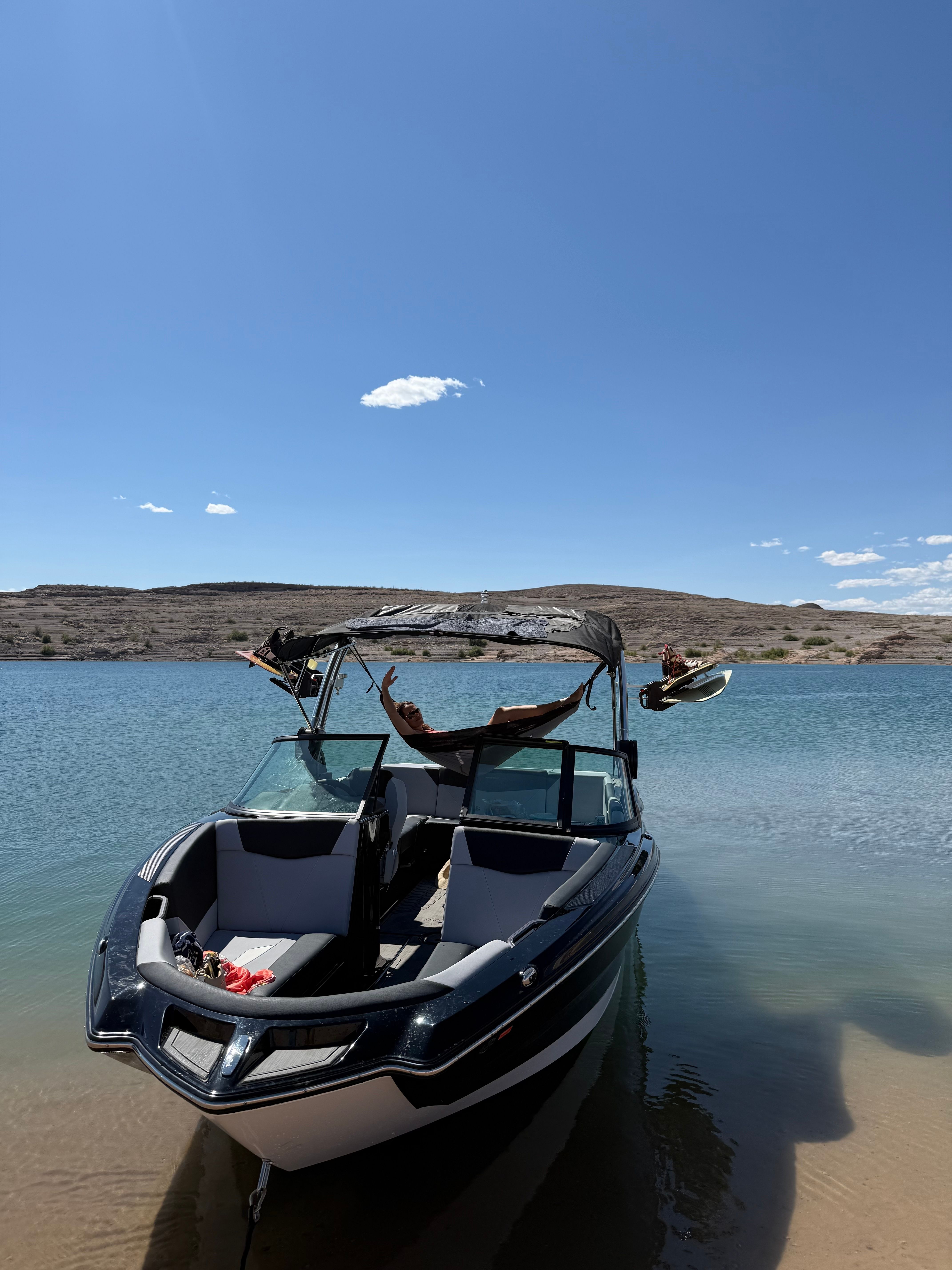 A MasterCraft NXT23 boat is on calm lake water under a clear sky.