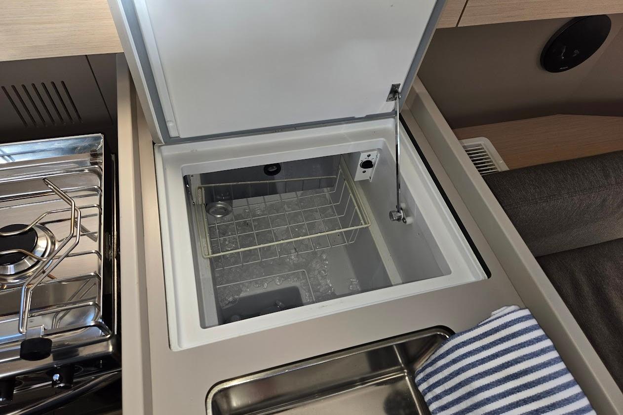 Beneteau Oceanis 38.1 yacht kitchen with open fridge, stove, and striped towel, 2023 model.
