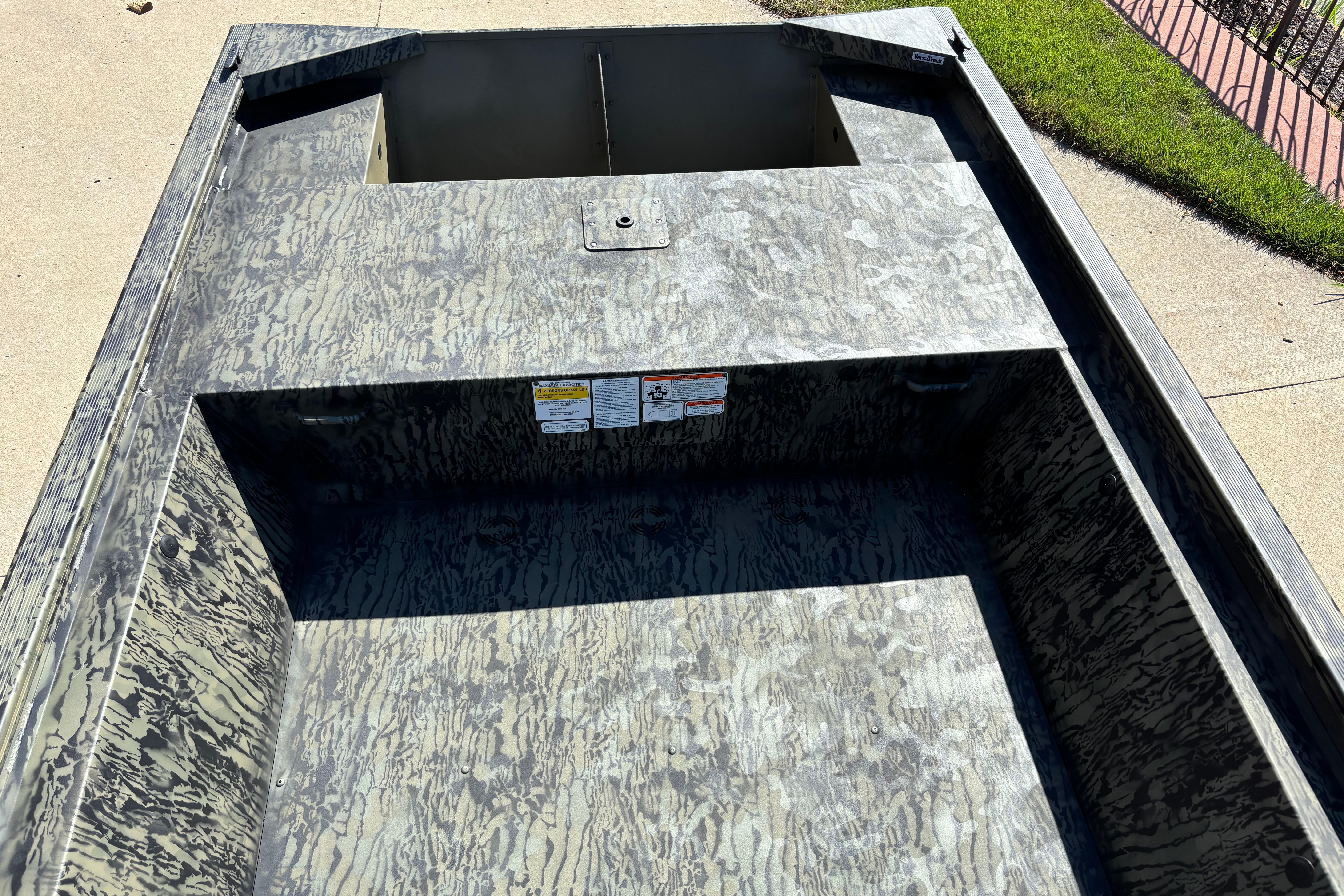 2026 Tracker Grizzly 1648 Utility boat with camouflage interior design, parked on concrete.