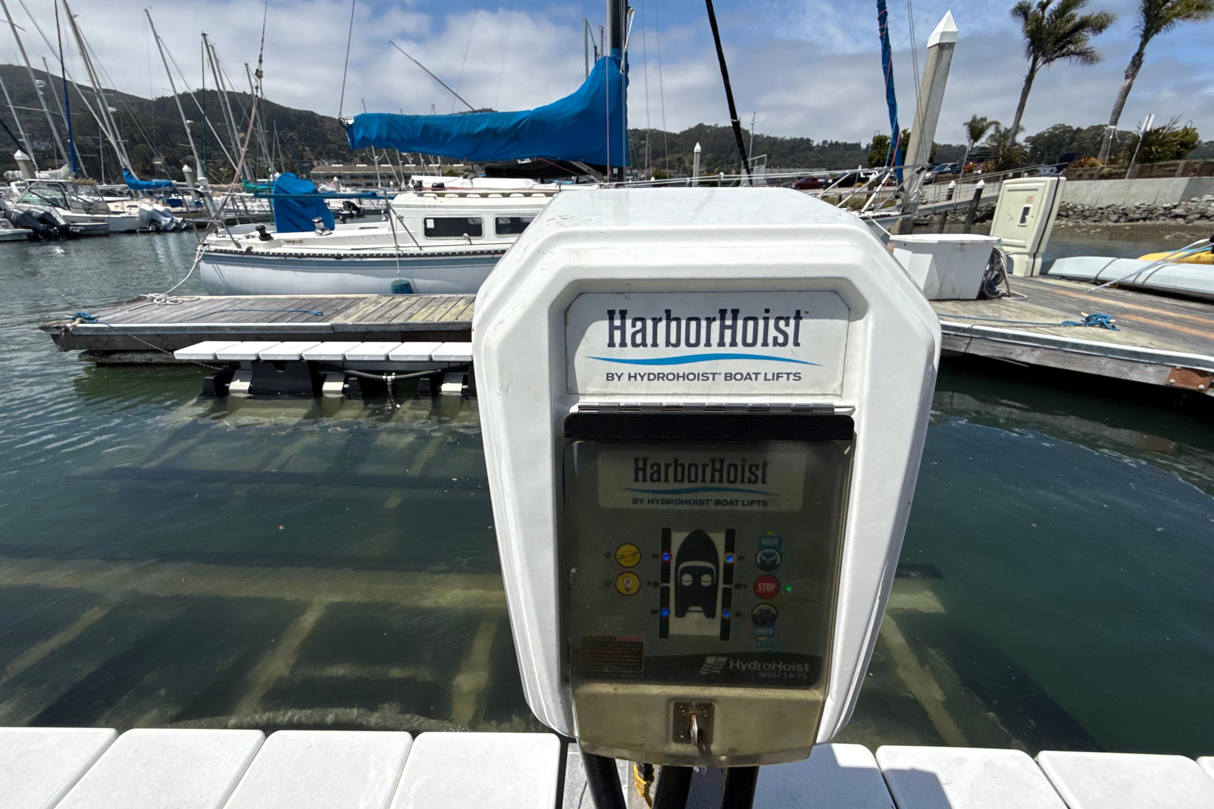 HarborHoist boat lift control panel at marina with docked sailboats in background.