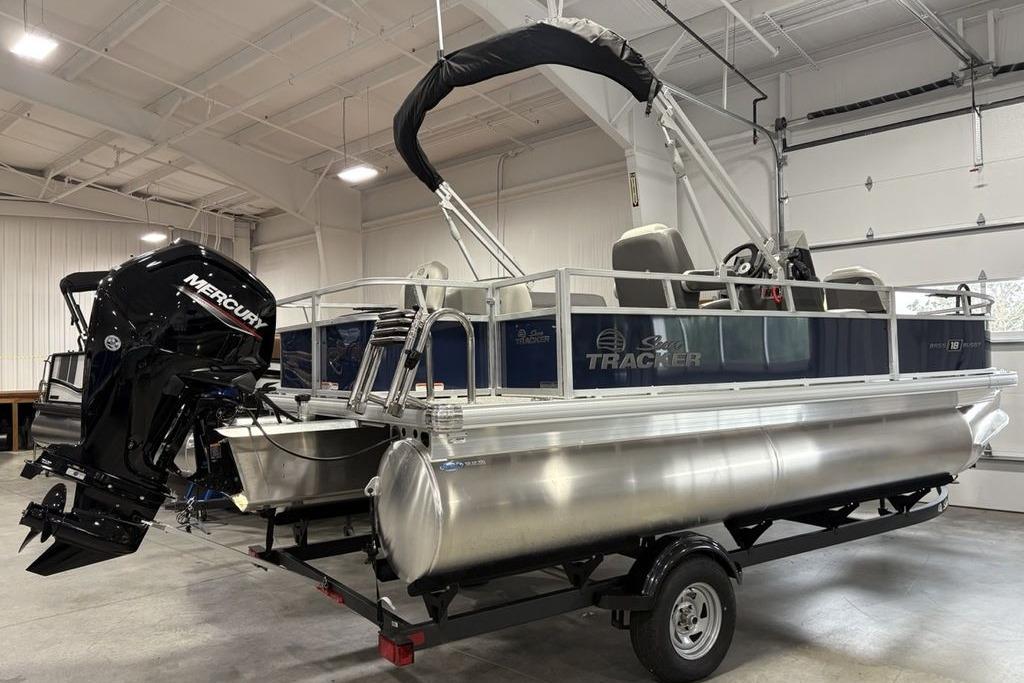 2026 Sun Tracker Bass Buggy 18 DLX pontoon boat with Mercury engine in a garage.