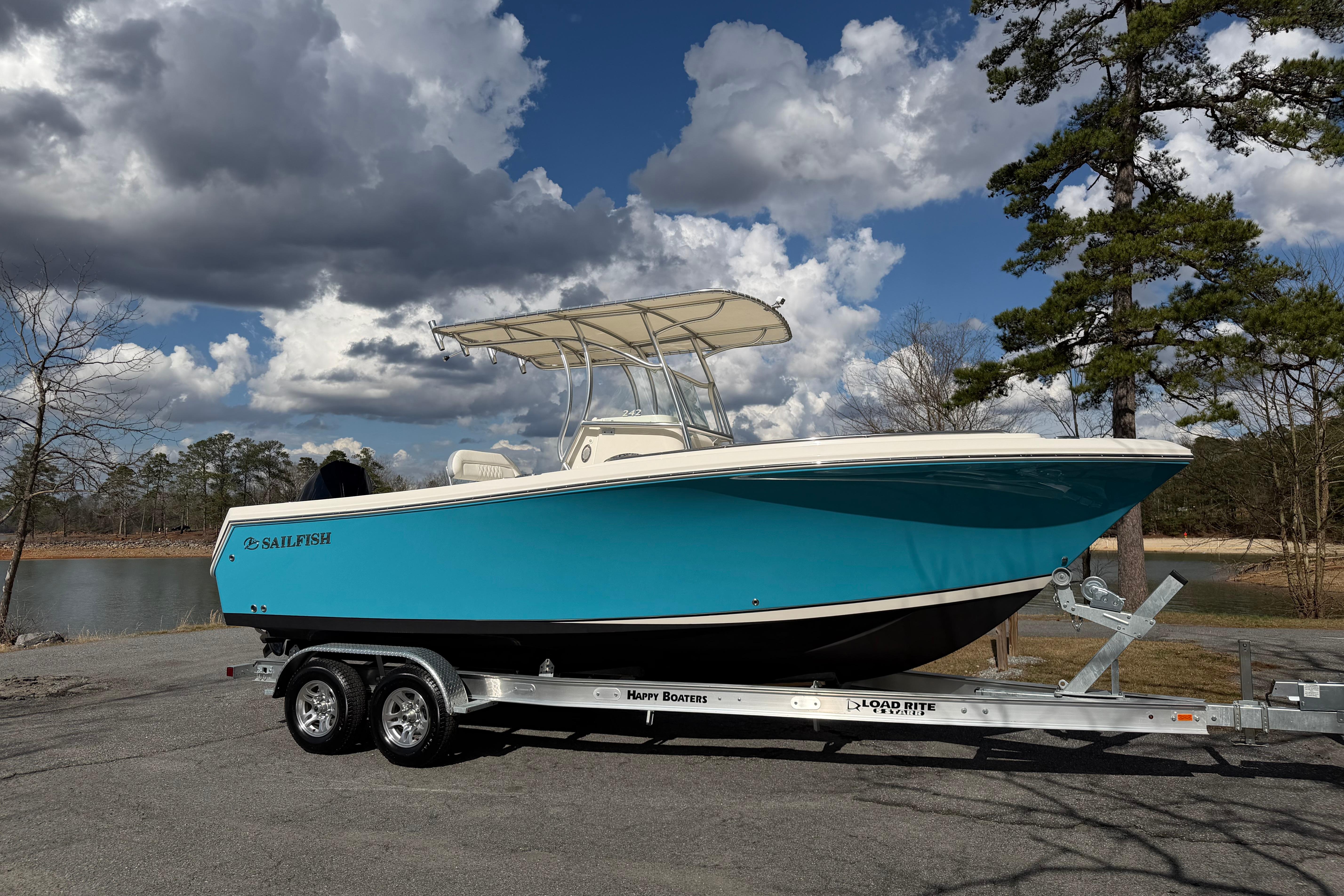 2022 Sailfish 242 CC boat on trailer, parked near a scenic lake under cloudy sky.