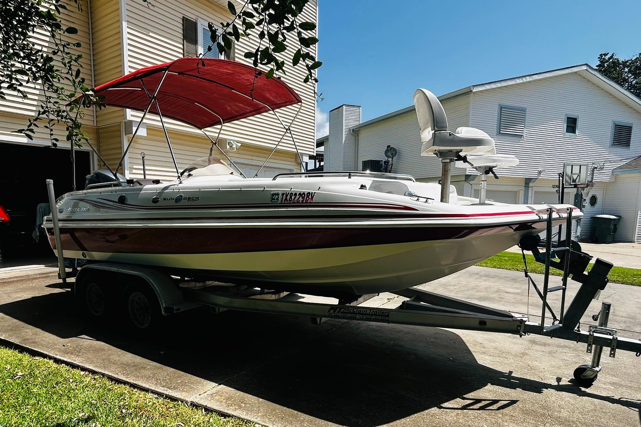 2013 Hurricane SunDeck Sport 201 OB boat on trailer with red canopy in residential driveway.
