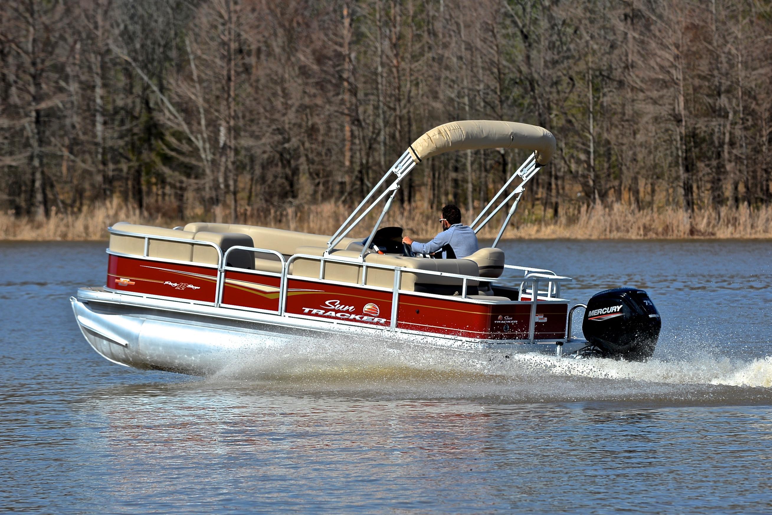 2023 Sun Tracker Party Barge 18 DLX cruising on a lake with forest backdrop.